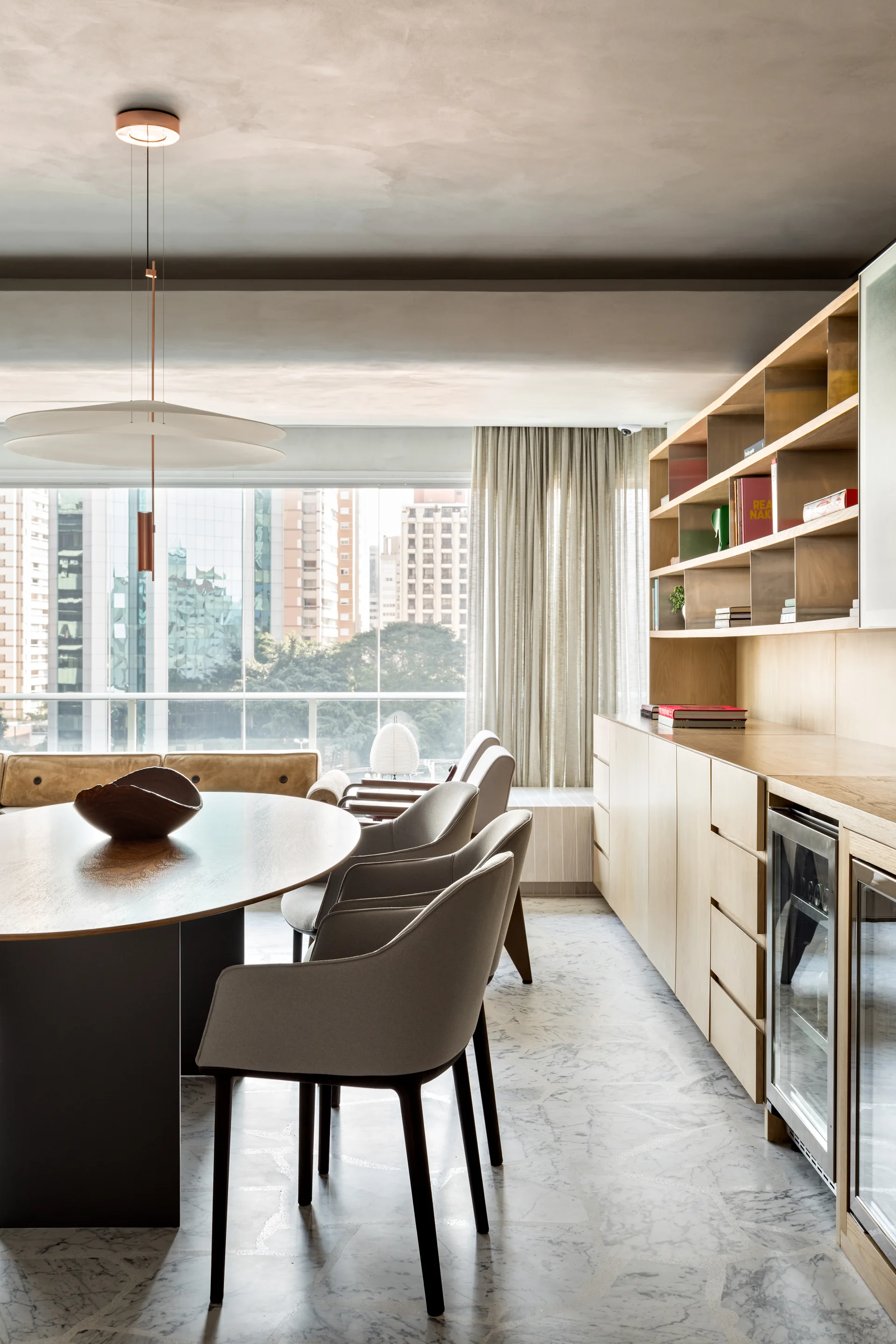 A contemporary dining room featuring an oval wood table, upholstered chairs, and a long built-in wooden sideboard under a plaster ceiling.