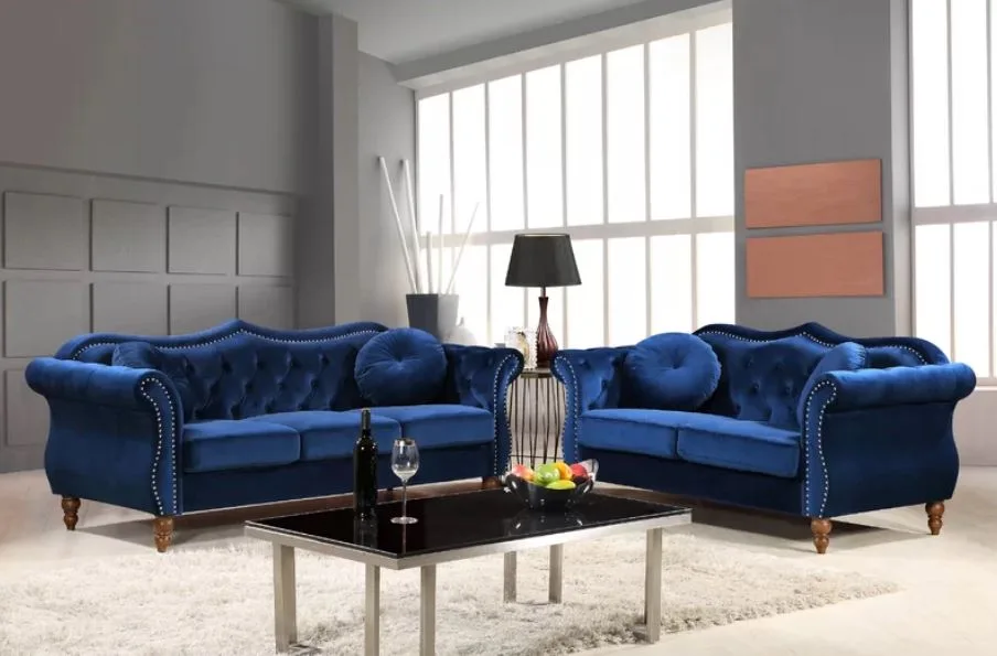 Two tufted navy blue velvet sofas sit on a cream shag rug around a black coffee table in front of a grey paneled wall.