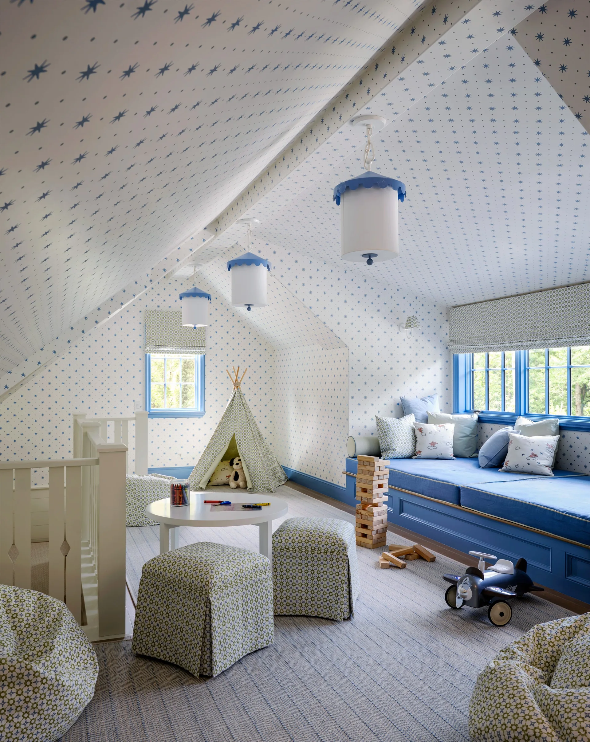 An attic playroom featuring sloped ceilings covered in blue star wallpaper, a built-in blue window seat, and small patterned ottomans.