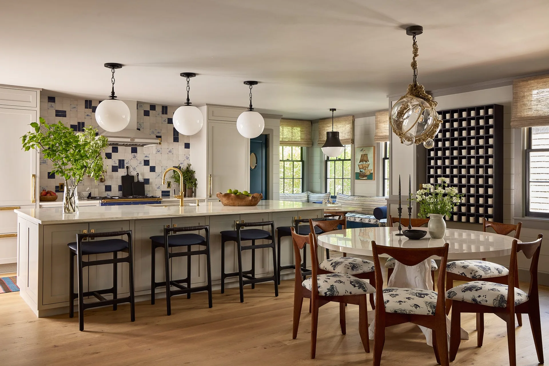 An open kitchen and dining space featuring a large island, blue and white tiled backsplash, globe pendants, and a round wooden dining set.