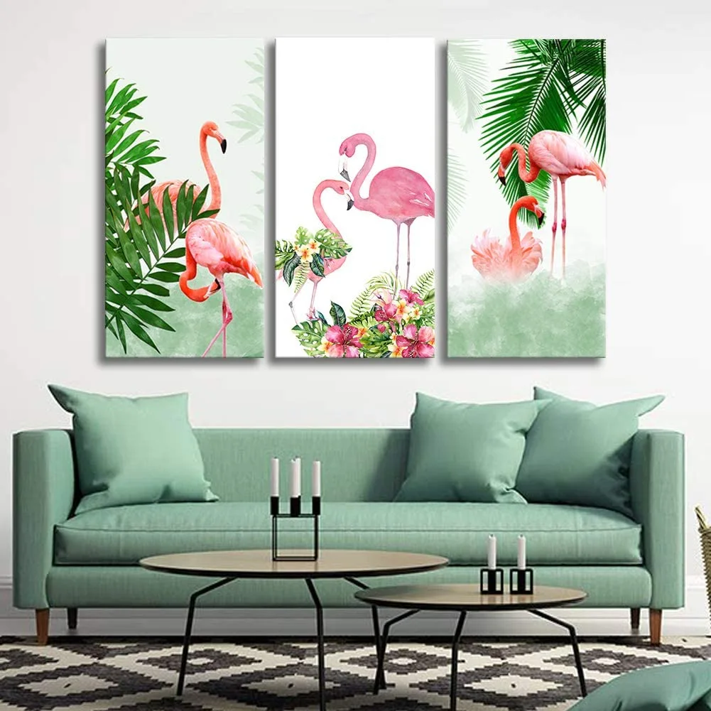 A sage green sofa sits beneath a three-panel flamingo art print, with two black nesting coffee tables on a geometric patterned rug.