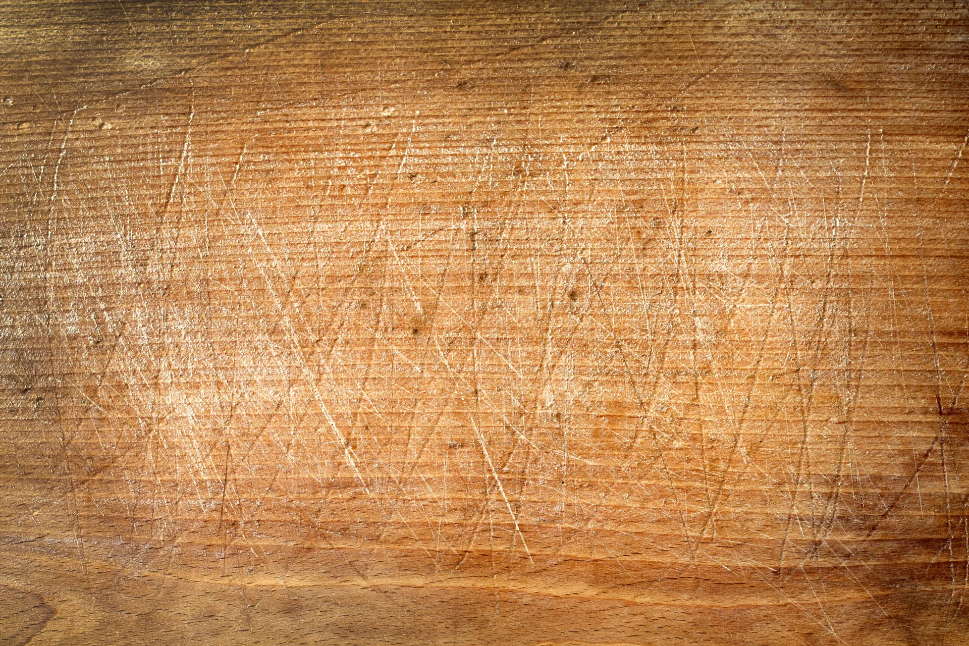 A close-up view of a warm brown wooden surface featuring horizontal grain lines and a heavily scratched distressed texture.