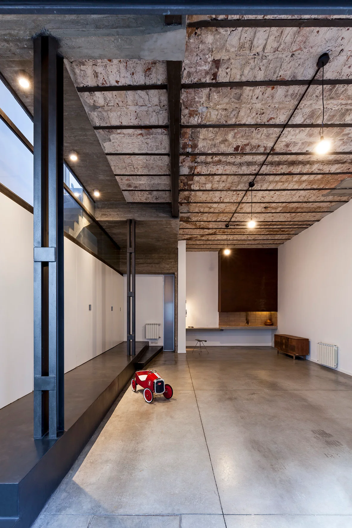 An open industrial room features a polished concrete floor, a textured brick ceiling with steel beams, and white built-in cabinets.