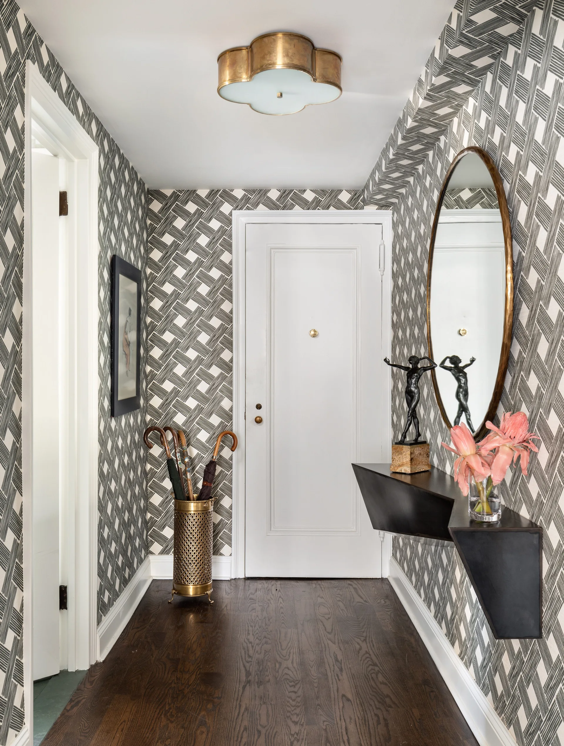A narrow entryway features bold black and white geometric wallpaper, a floating black console, and a brass scalloped ceiling light.