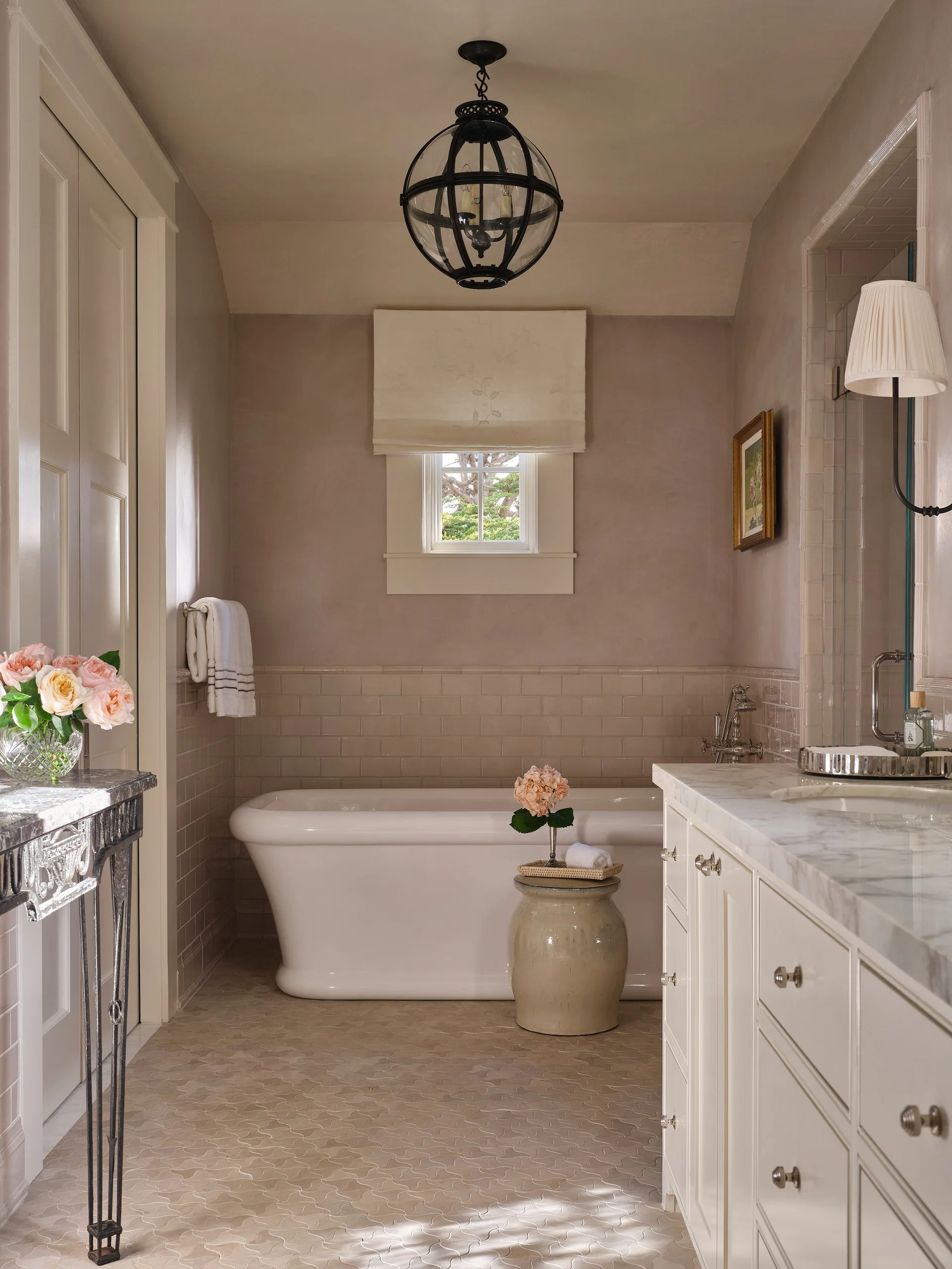 A transitional bathroom features a white freestanding bathtub, a marble-topped vanity, a ceramic garden stool, and a black lantern pendant light.