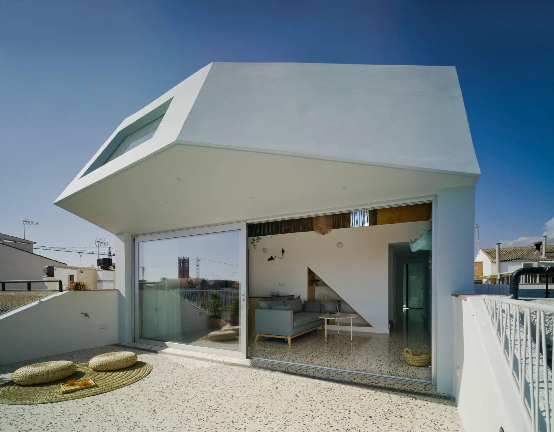 A modern rooftop patio with a white geometric exterior, speckled terrazzo flooring, and a sliding glass door opening to an indoor living area.