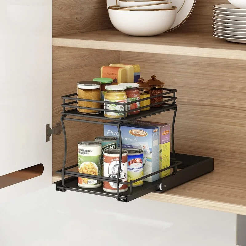A two-tier black metal pull-out shelf filled with jars and canned food sits inside a light wood cabinet.