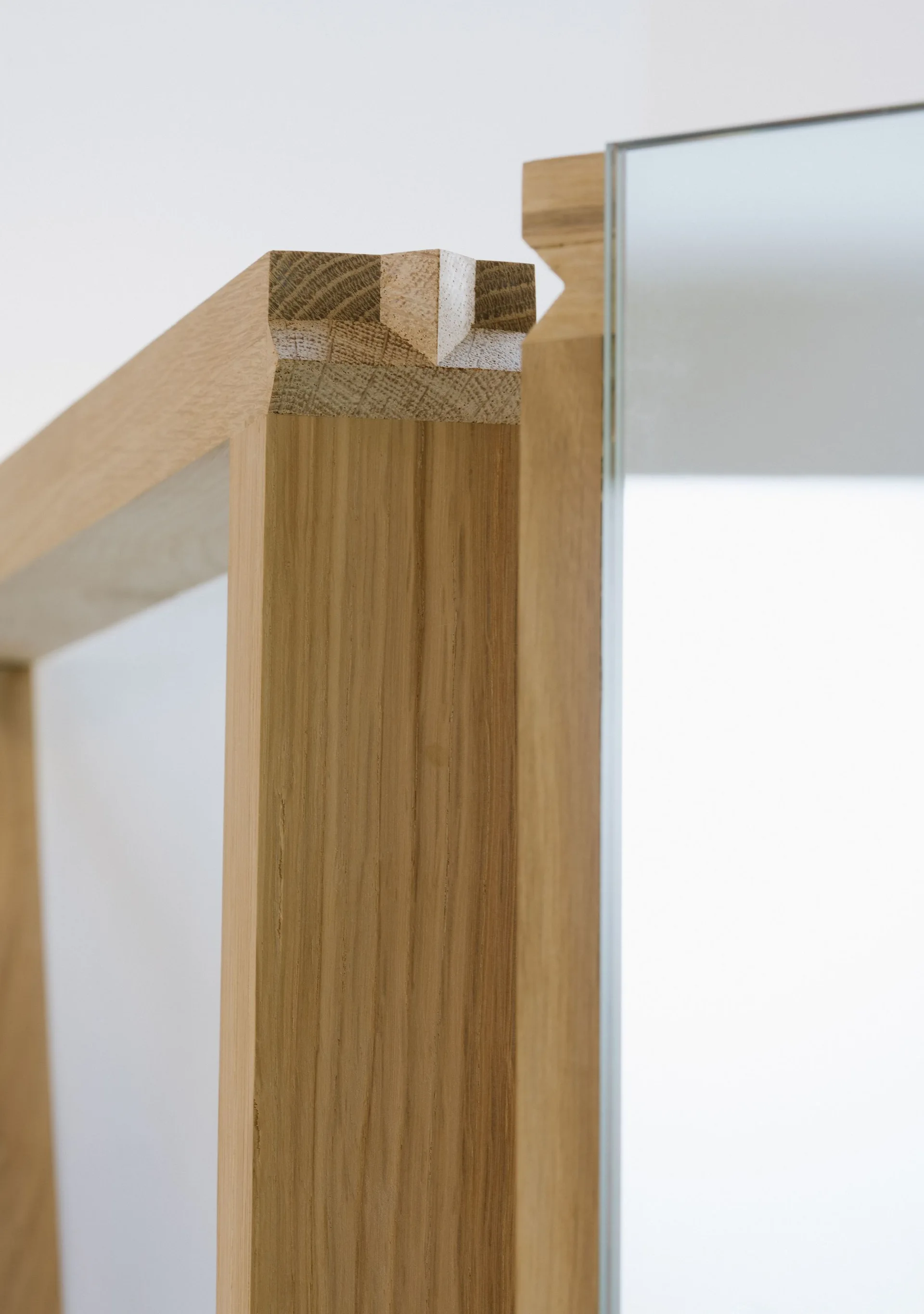A close-up shot of a light-colored wooden mirror frame showcasing the intricate interlocking joinery detail at the corner.