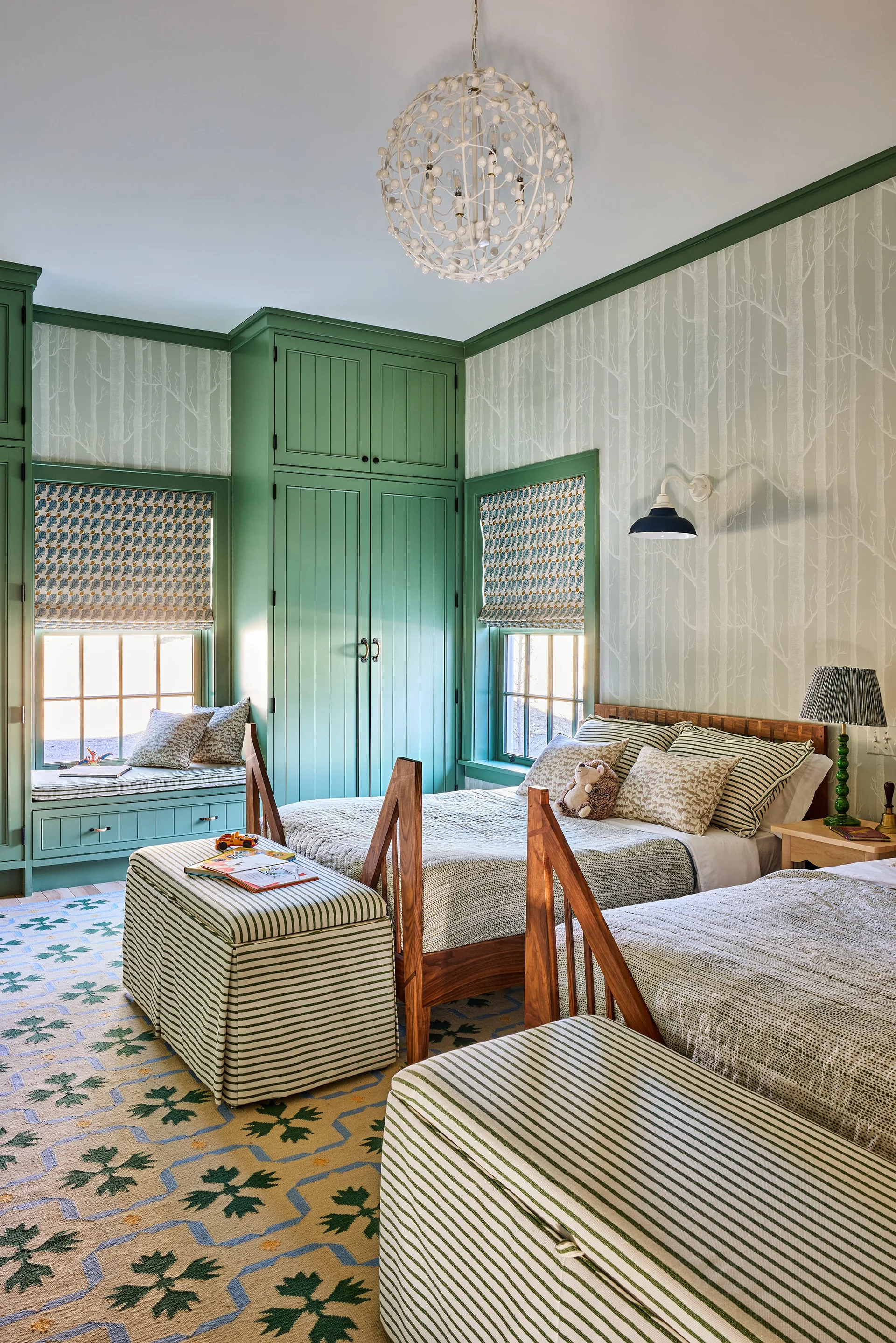 A cozy shared children's bedroom featuring twin beds with striped bedding, green built-in wardrobes, and tree-patterned wallpaper.