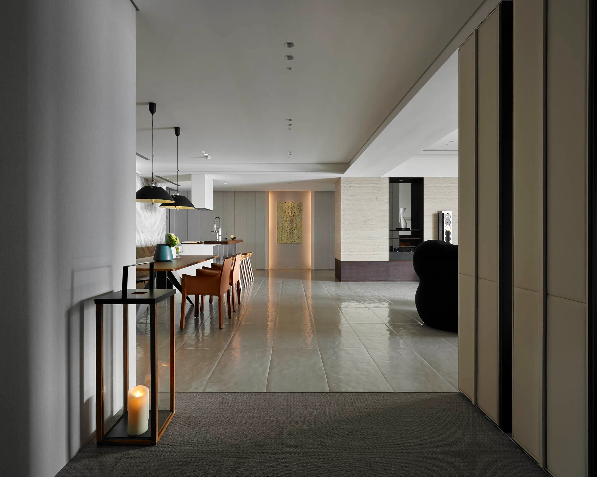 A contemporary open-plan dining area features tan leather chairs, black pendant lights, and glossy grey tile floors reflecting warm light.