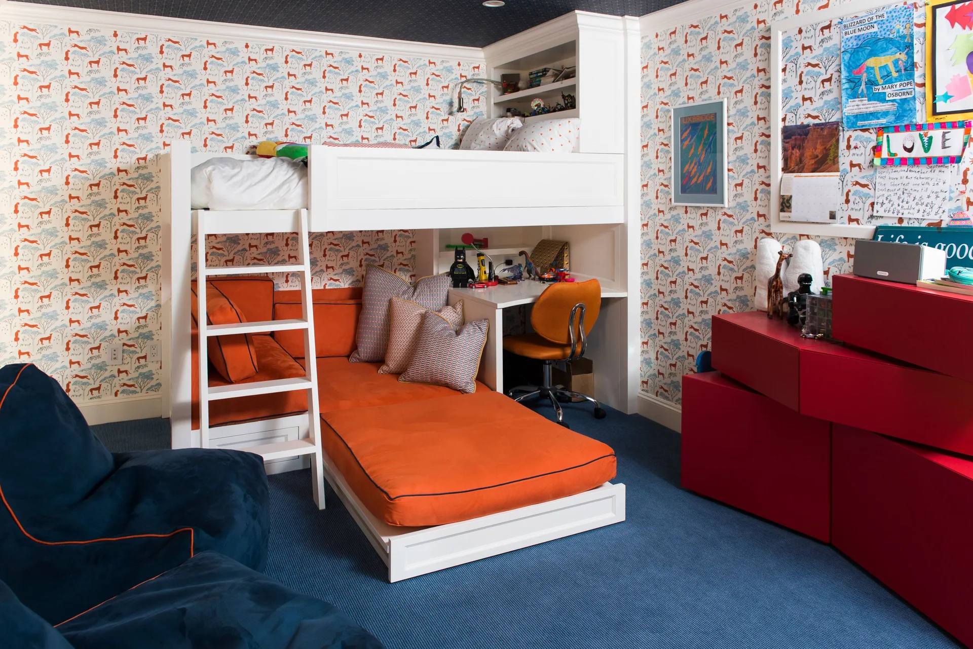 A child's bedroom featuring a white loft bed over an orange couch and desk, animal print wallpaper, and red storage cabinets.