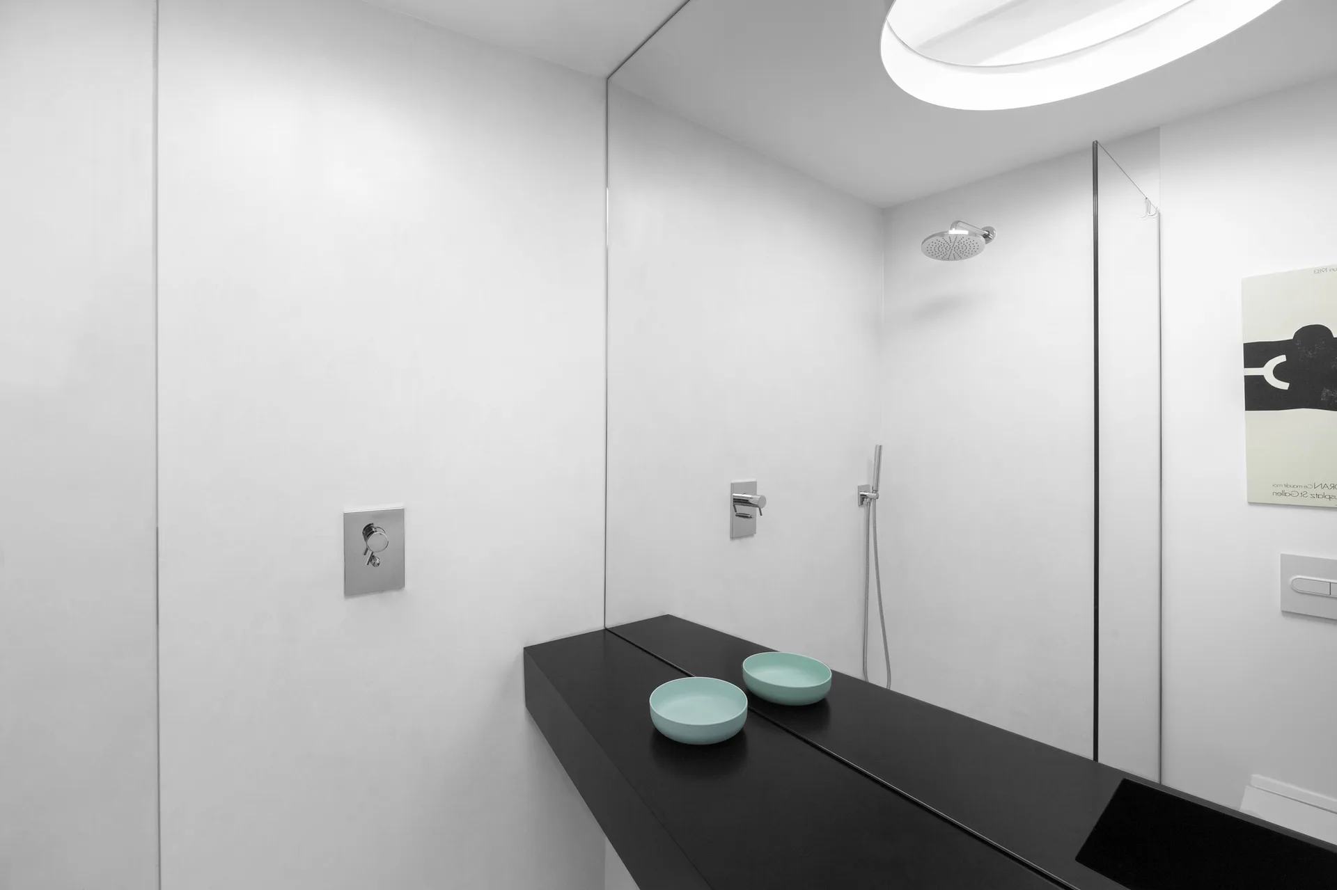 A minimalist bathroom features a matte black floating vanity set against a seamless wall-to-wall mirror with light blue decorative bowls.