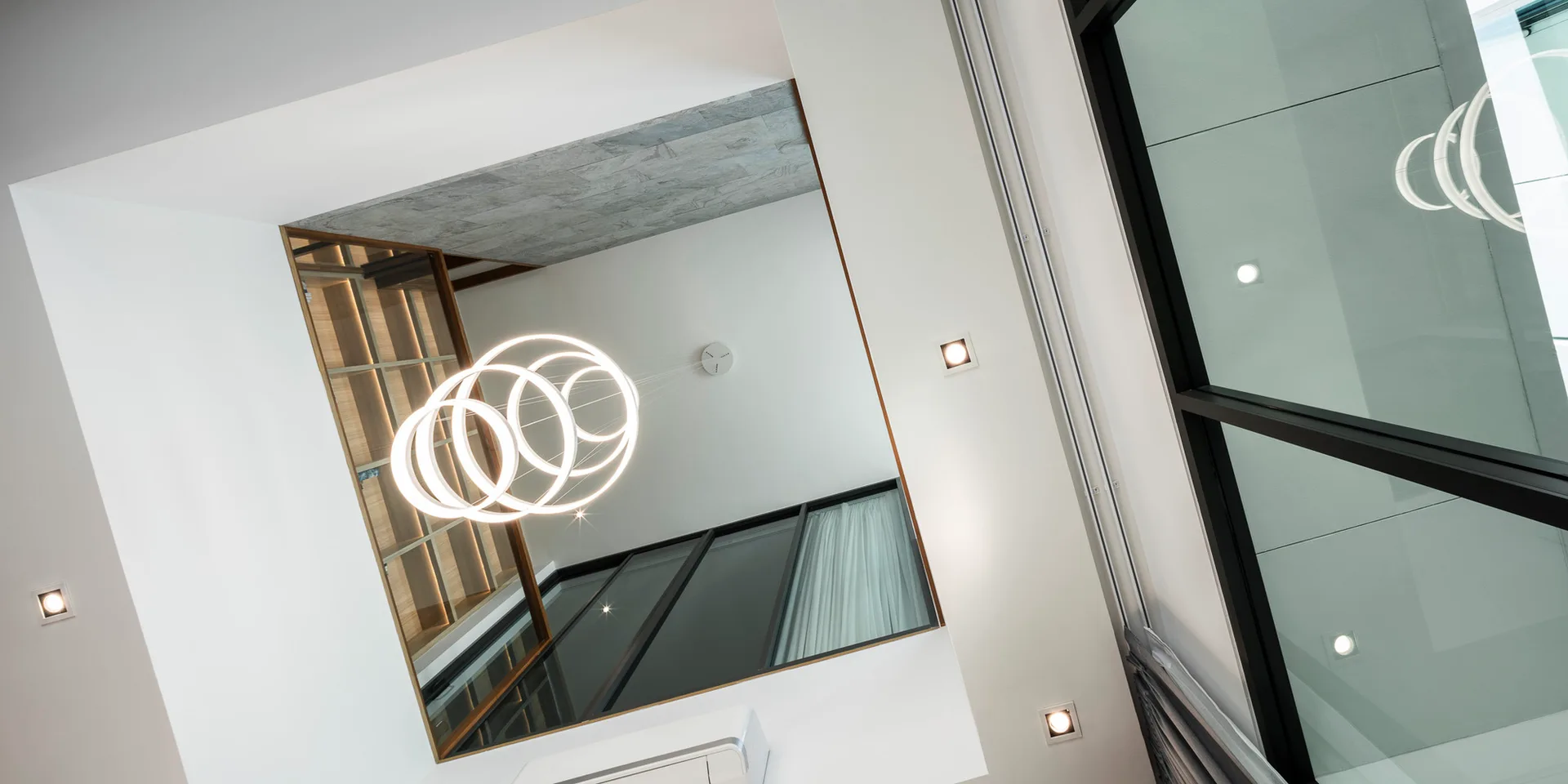 Low-angle view of a white ceiling with an architectural recess, a modern circular ring pendant light, and a glass partition.