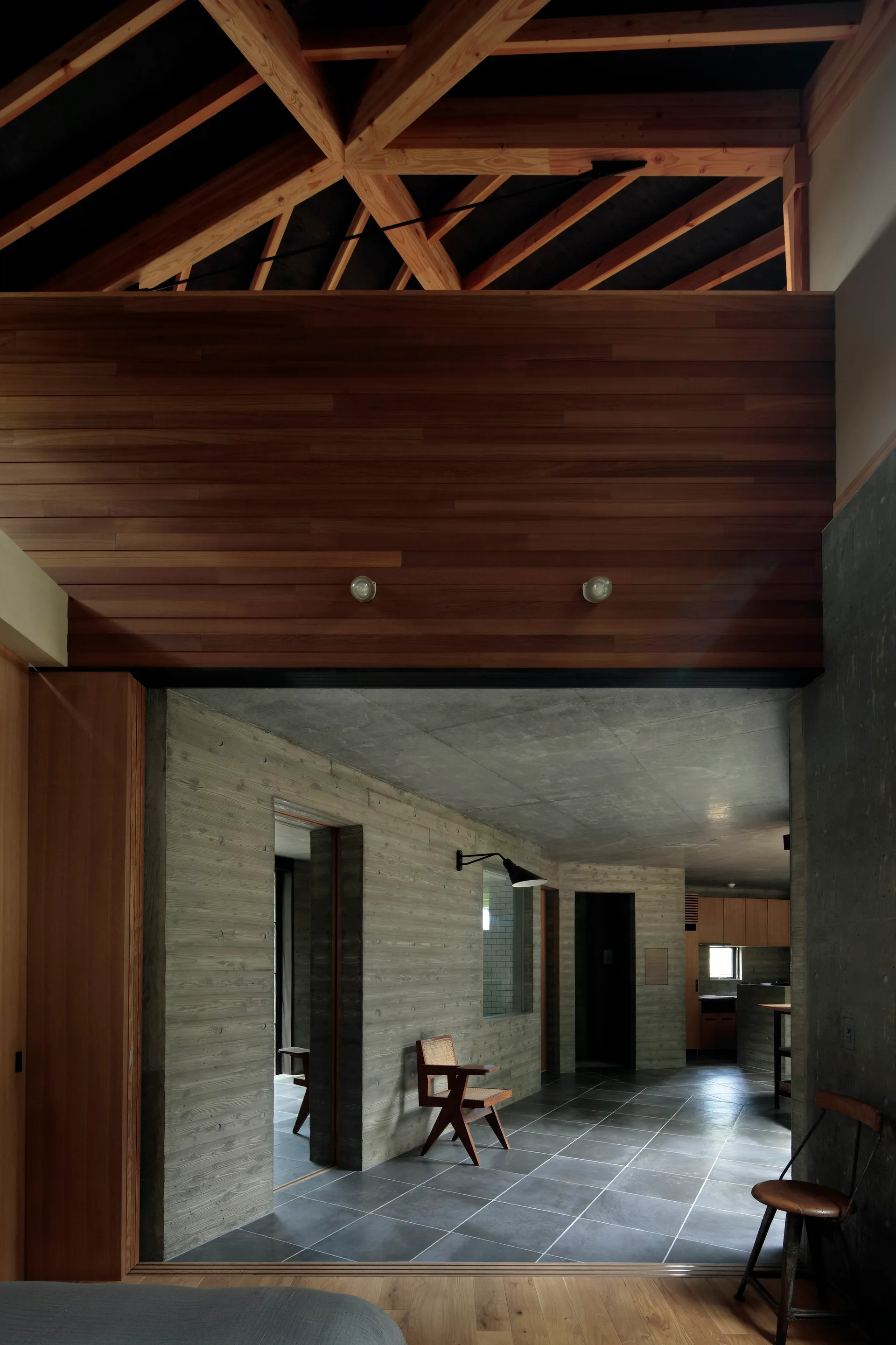 An interior hallway with textured concrete walls, a dark tiled floor, and a vaulted wooden truss ceiling.