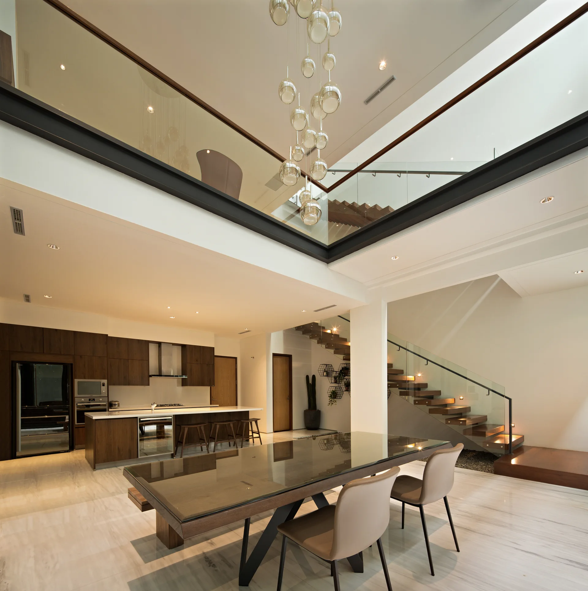 A double-height modern dining area features a glass-topped table, a floating wooden staircase with glass railings, and an open kitchen with dark wood cabinets.