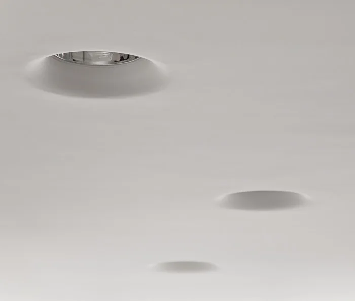 A close-up of three trimless circular recessed lights integrated into a smooth matte white plaster ceiling.