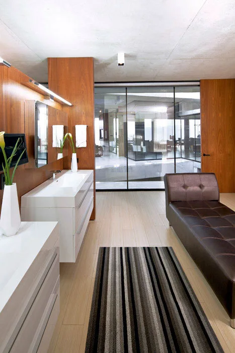 A modern bathroom featuring a white wall-mounted vanity, a brown tufted leather chaise lounge, and warm wood-paneled walls.