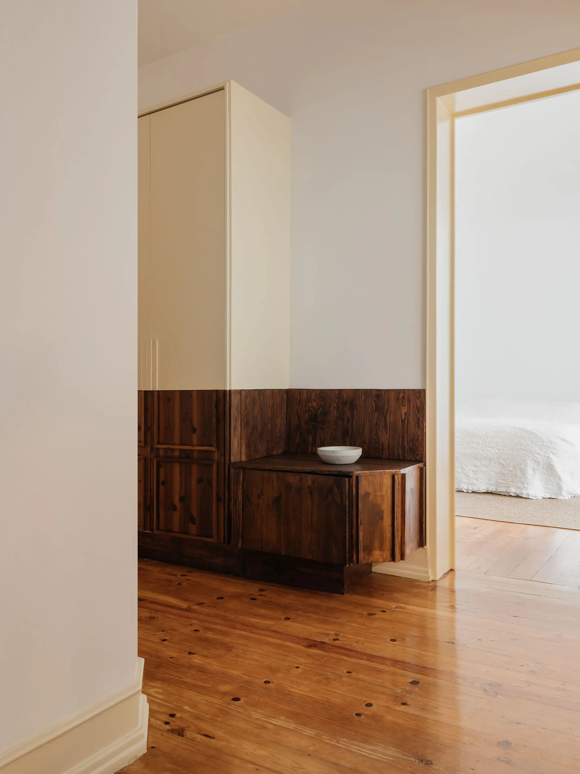 A hallway features custom built-in storage with off-white upper cabinets and dark wood-grained lower paneling next to a doorway.