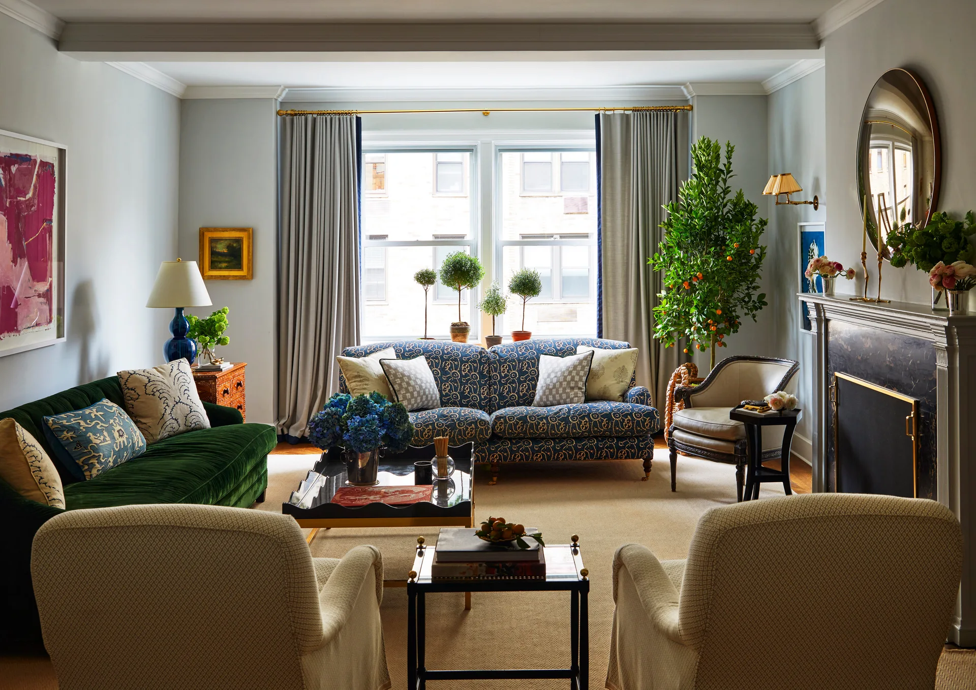 A traditional living room with a green velvet sofa, a blue patterned couch by a window, a fireplace, and two beige armchairs.