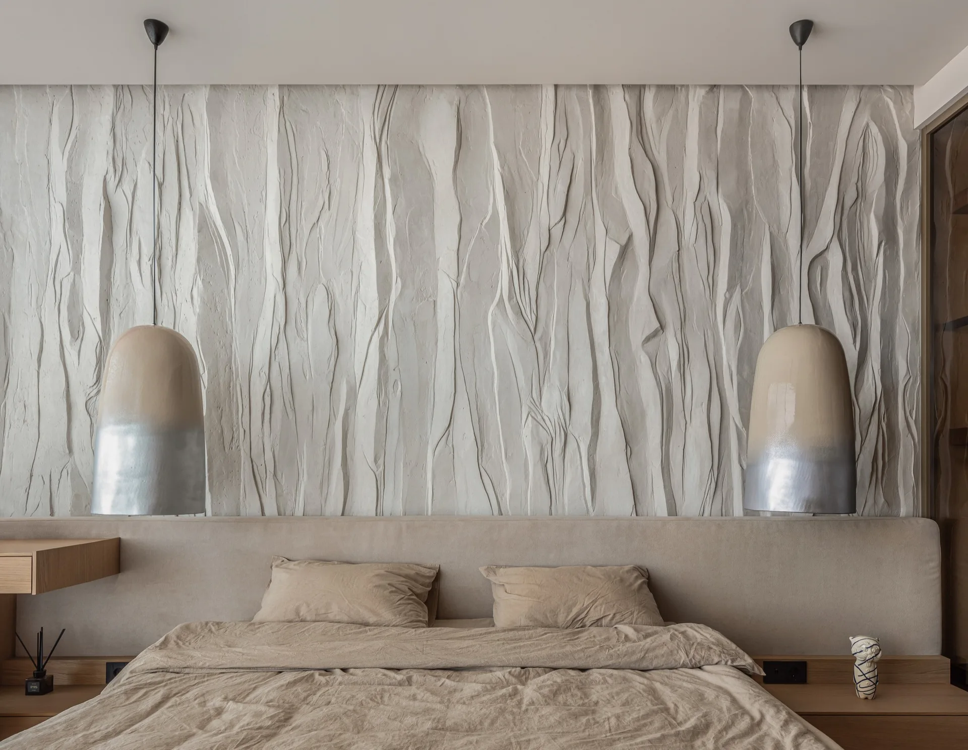 A modern bedroom features a heavily textured plaster accent wall behind a low beige headboard flanked by two-tone pendant lights.