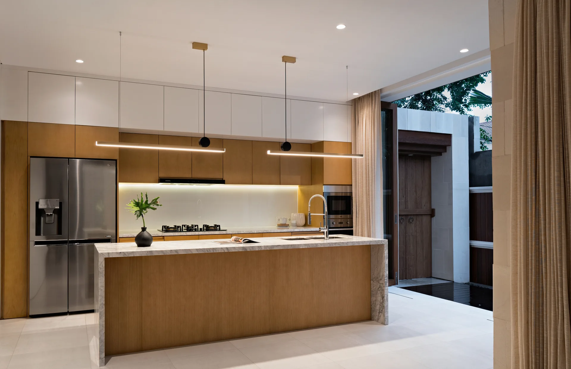 A minimalist kitchen features a marble waterfall island, wood and white flat-panel cabinetry, and sleek linear pendant lights.