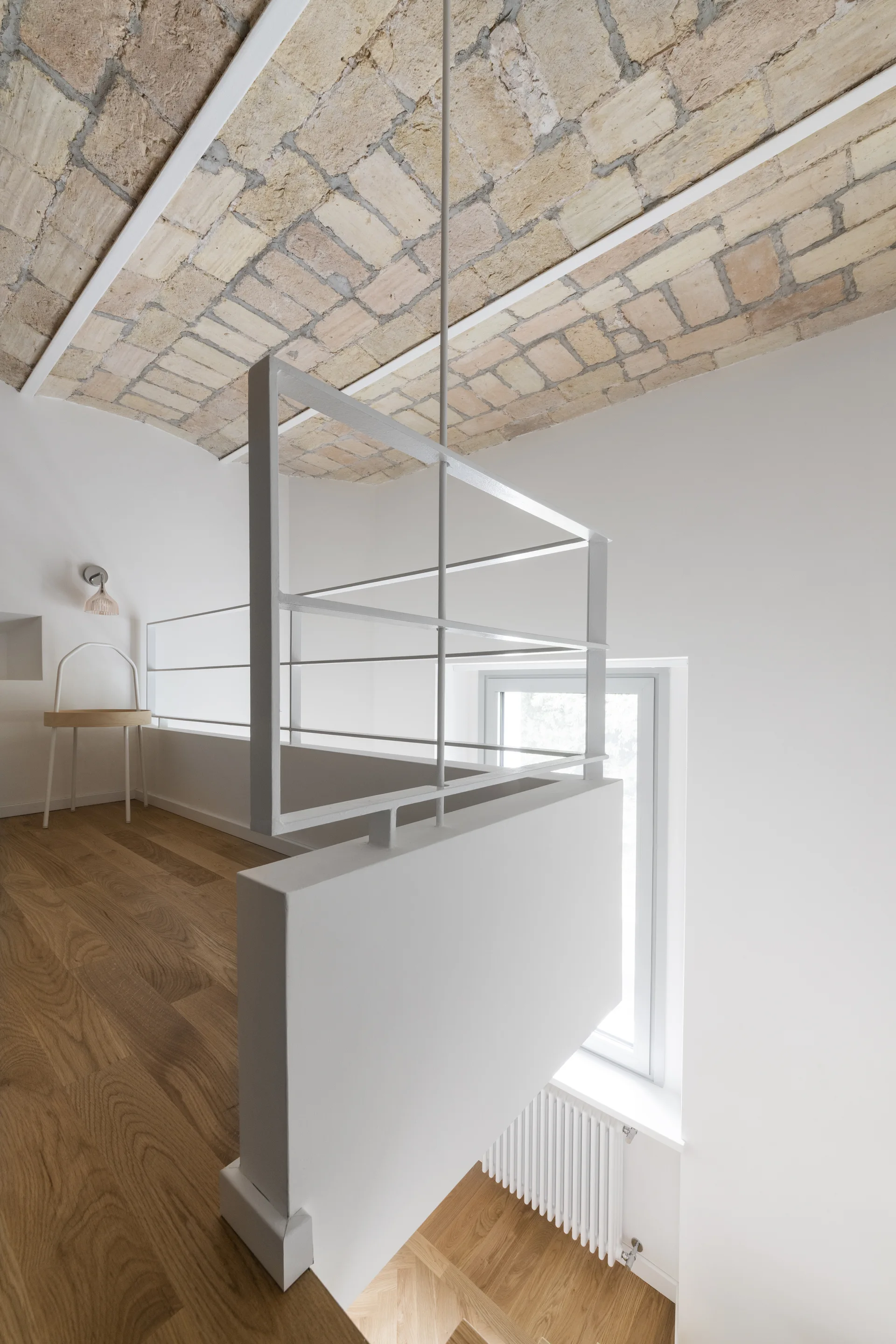 A mezzanine landing features a white metal railing, light wood flooring, and an arched, exposed brick barrel-vaulted ceiling.