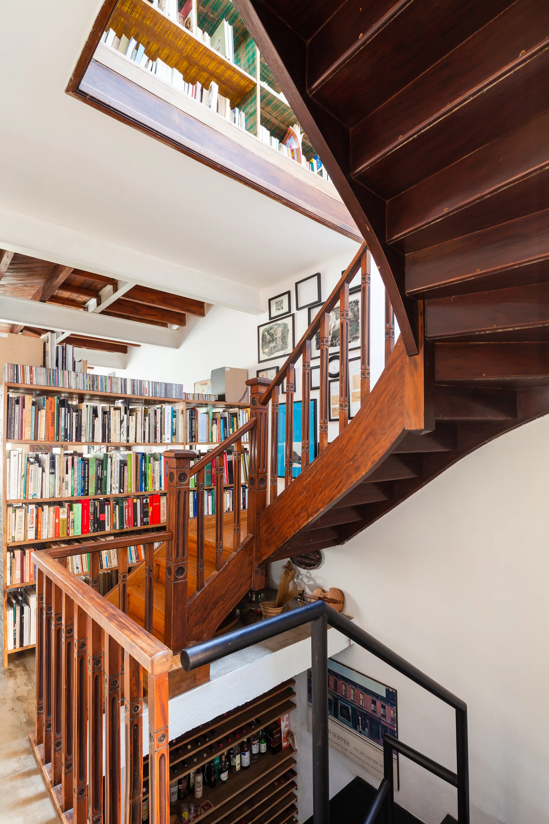 A dark wood multi-level staircase wraps around built-in bookshelves filled with books, set against clean white walls.
