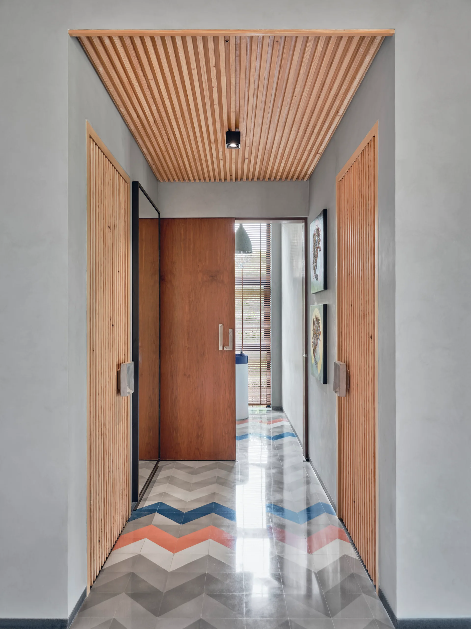 A modern hallway features glossy chevron-patterned floor tiles, a slatted wood ceiling, and integrated wooden doors set into smooth grey walls.