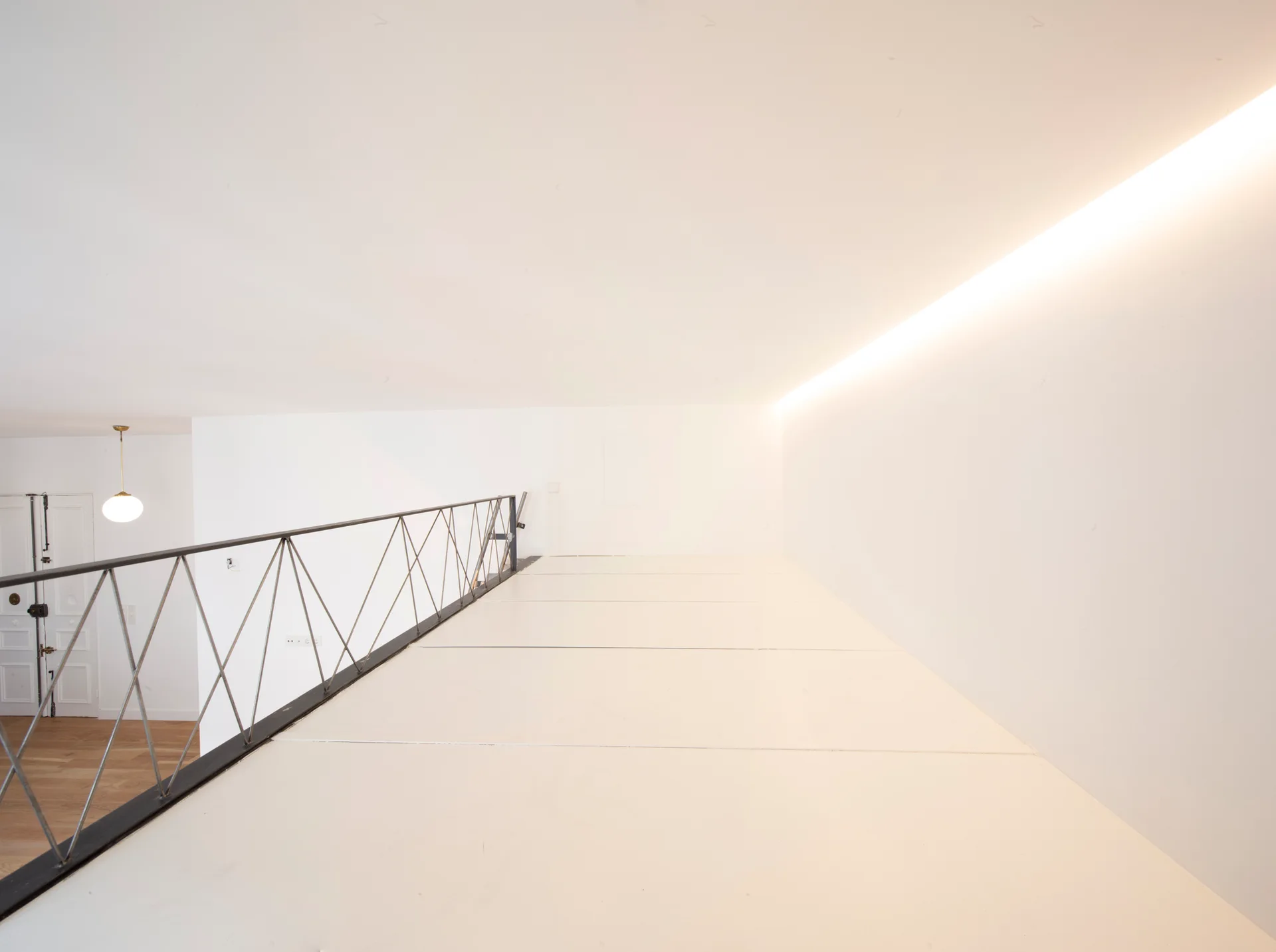 A white minimalist mezzanine landing features a black geometric metal railing and a linear glowing cove light along the ceiling edge.