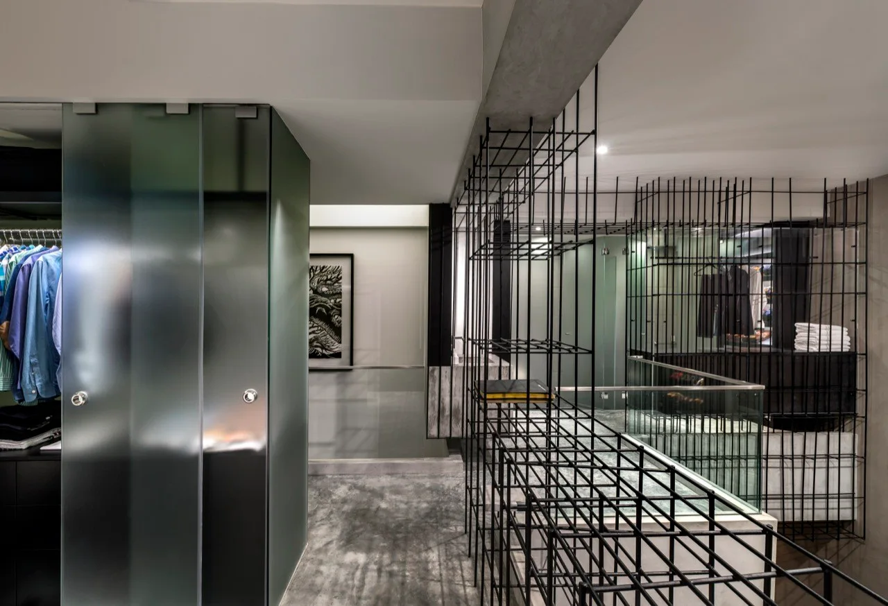 A modern closet space with frosted glass wardrobe doors next to a black metal grid partition and polished concrete flooring.