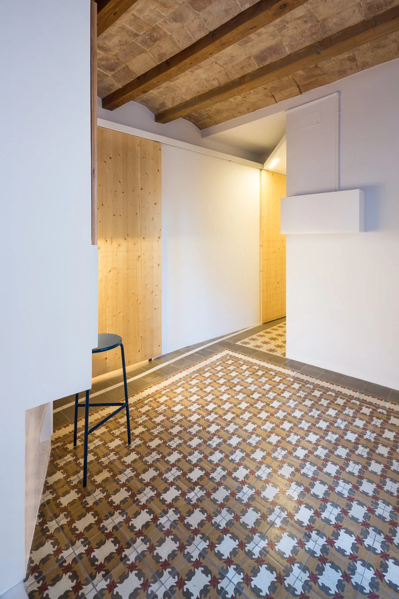 A modern hallway features a vaulted brick ceiling with wooden beams, light wood sliding doors, and intricate patterned floor tiles.