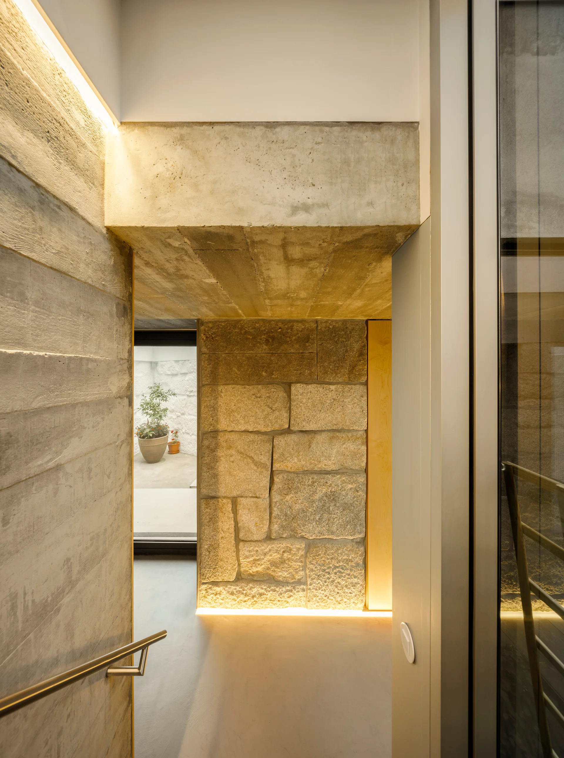 A modern concrete hallway features a textured board-formed wall, a rough stone block wall, and warm integrated strip lighting along the floor.