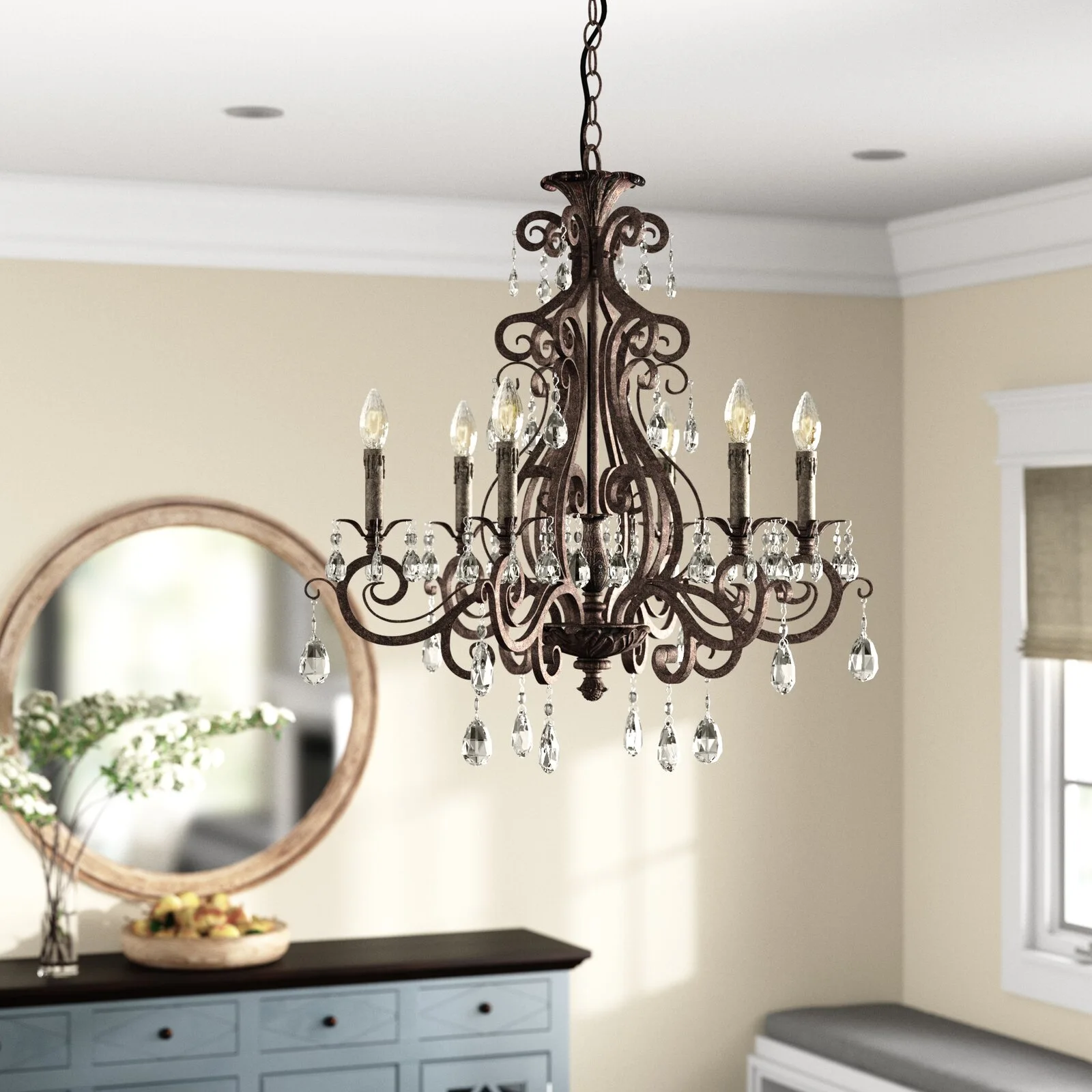 An ornate bronze chandelier with crystal drops hangs in a dining room featuring a round wooden mirror and a blue sideboard.