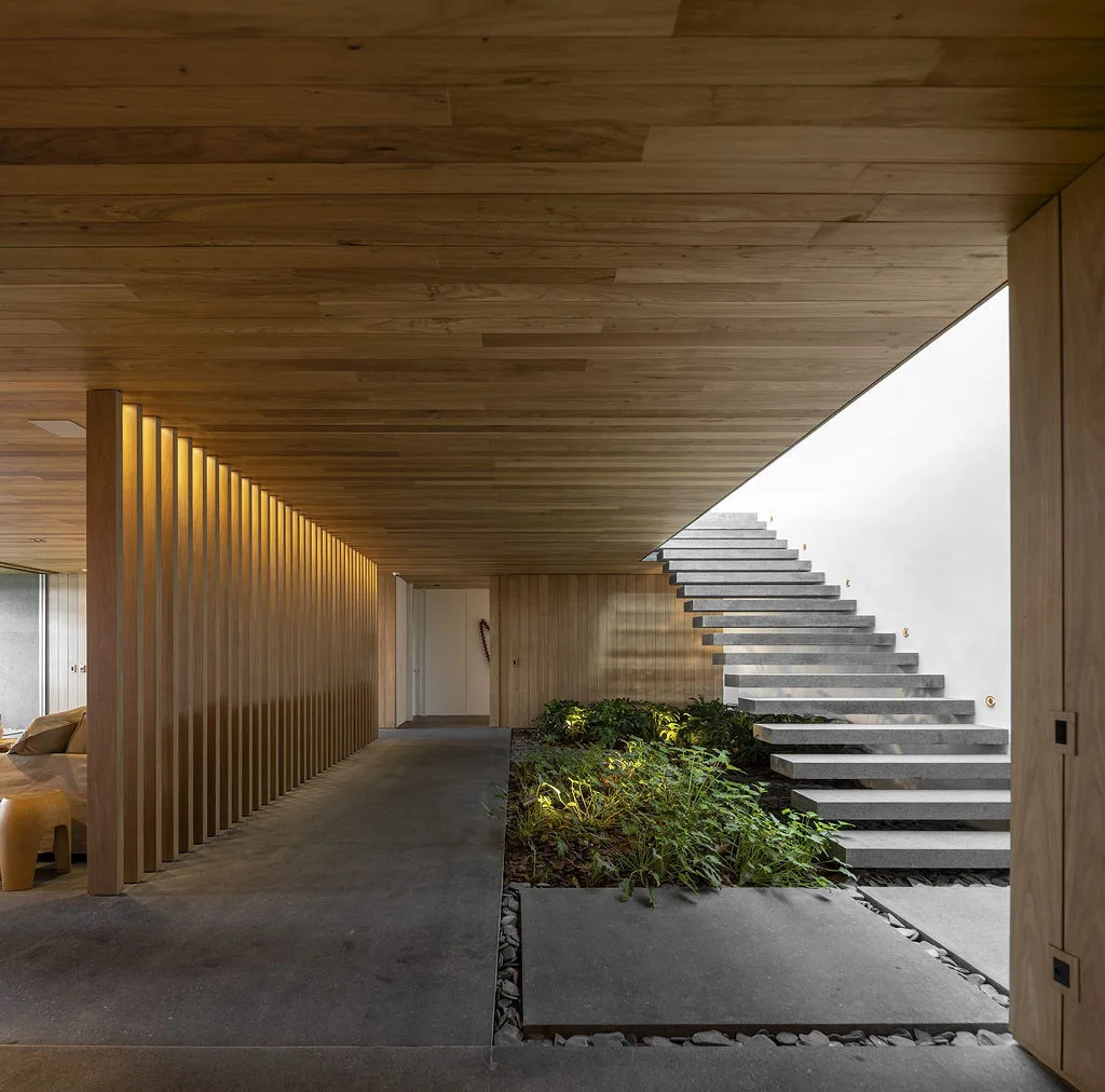 A minimalist architectural foyer with a floating stone staircase, an indoor garden, a slatted wood wall divider, and grey stone flooring.