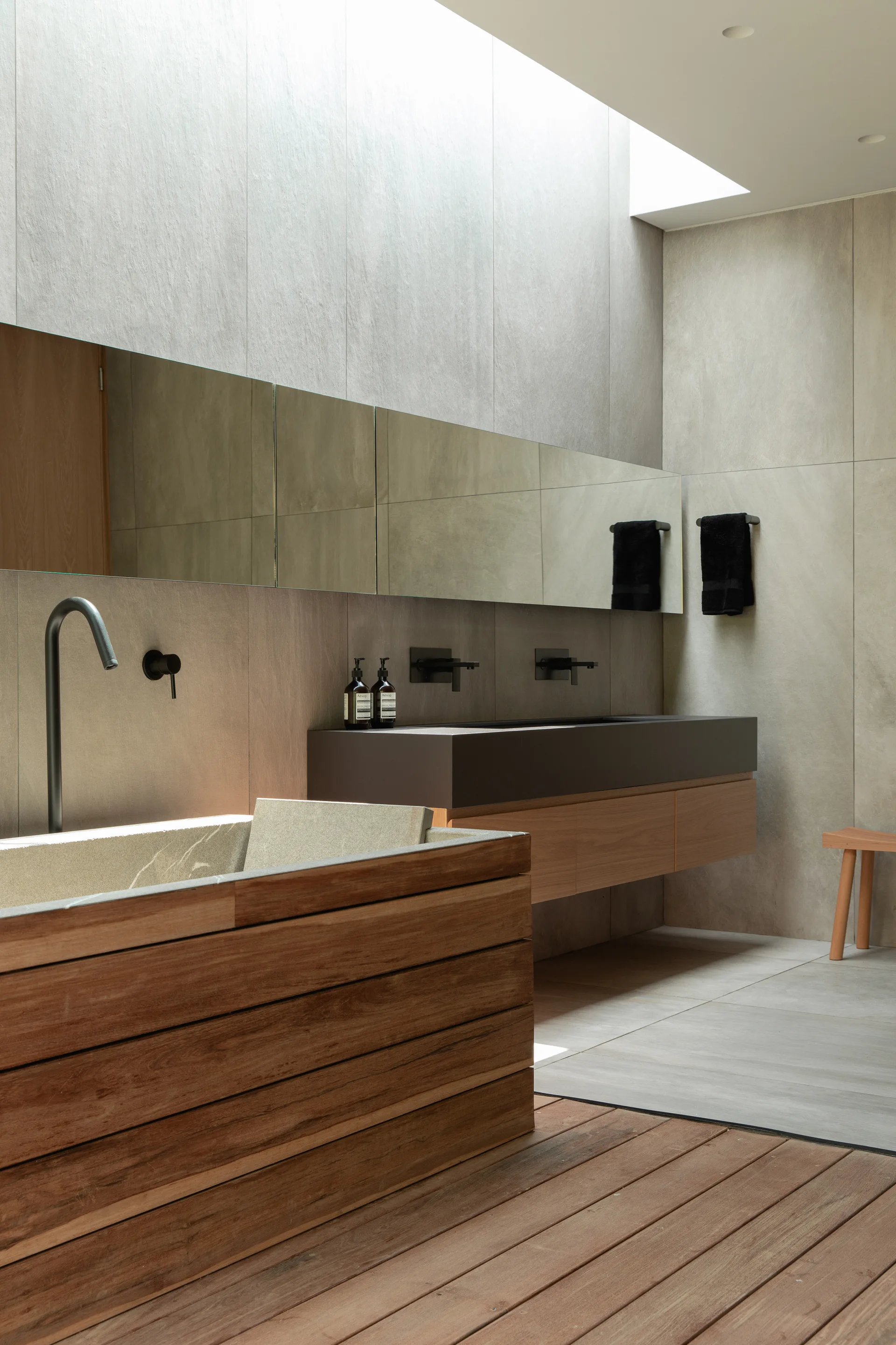 A modern bathroom features a wood-clad bathtub on a wood plank floor alongside a floating vanity under a bright skylight.