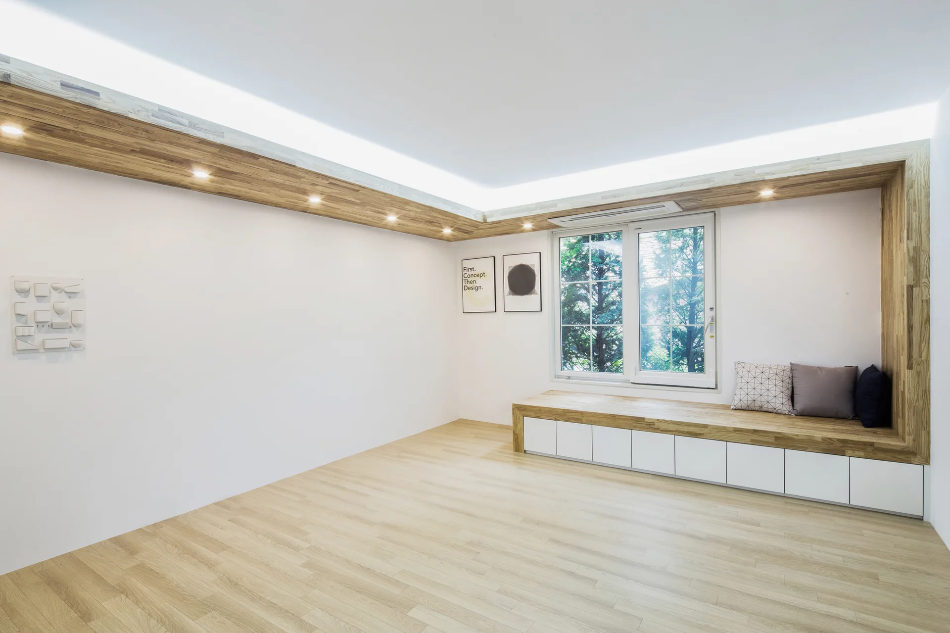 A minimalist room featuring a built-in wood window bench with white cabinets and a matching wood ceiling soffit with recessed downlights.