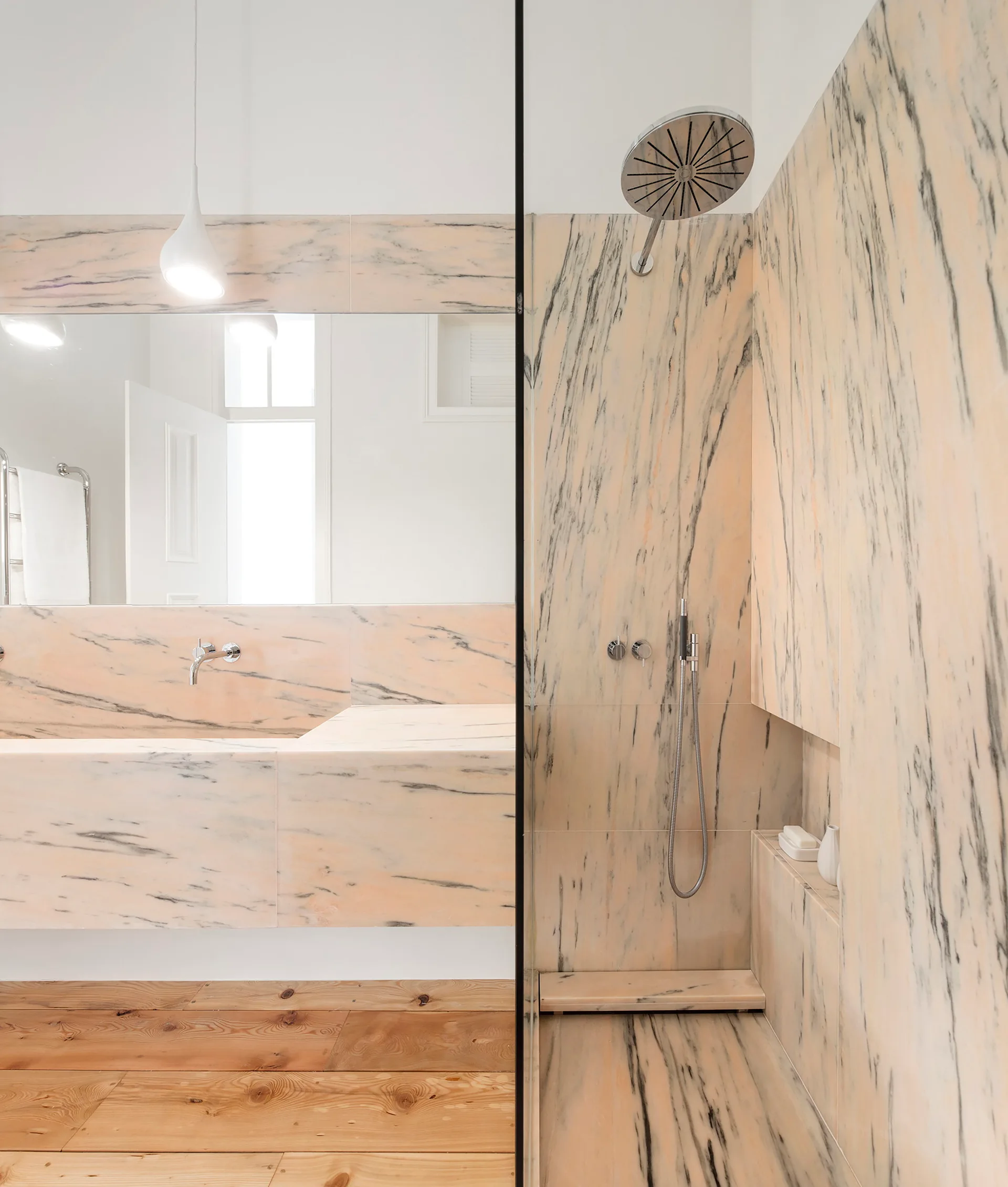 A modern bathroom features a pink veined marble vanity and walk-in shower contrasted by warm wood plank flooring.