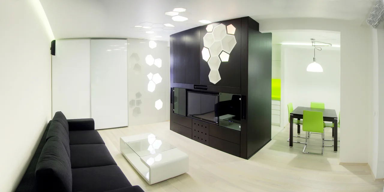 Modern living room with a black sofa, a white gloss coffee table, a dark media console with hexagonal panels, and bright green dining chairs.