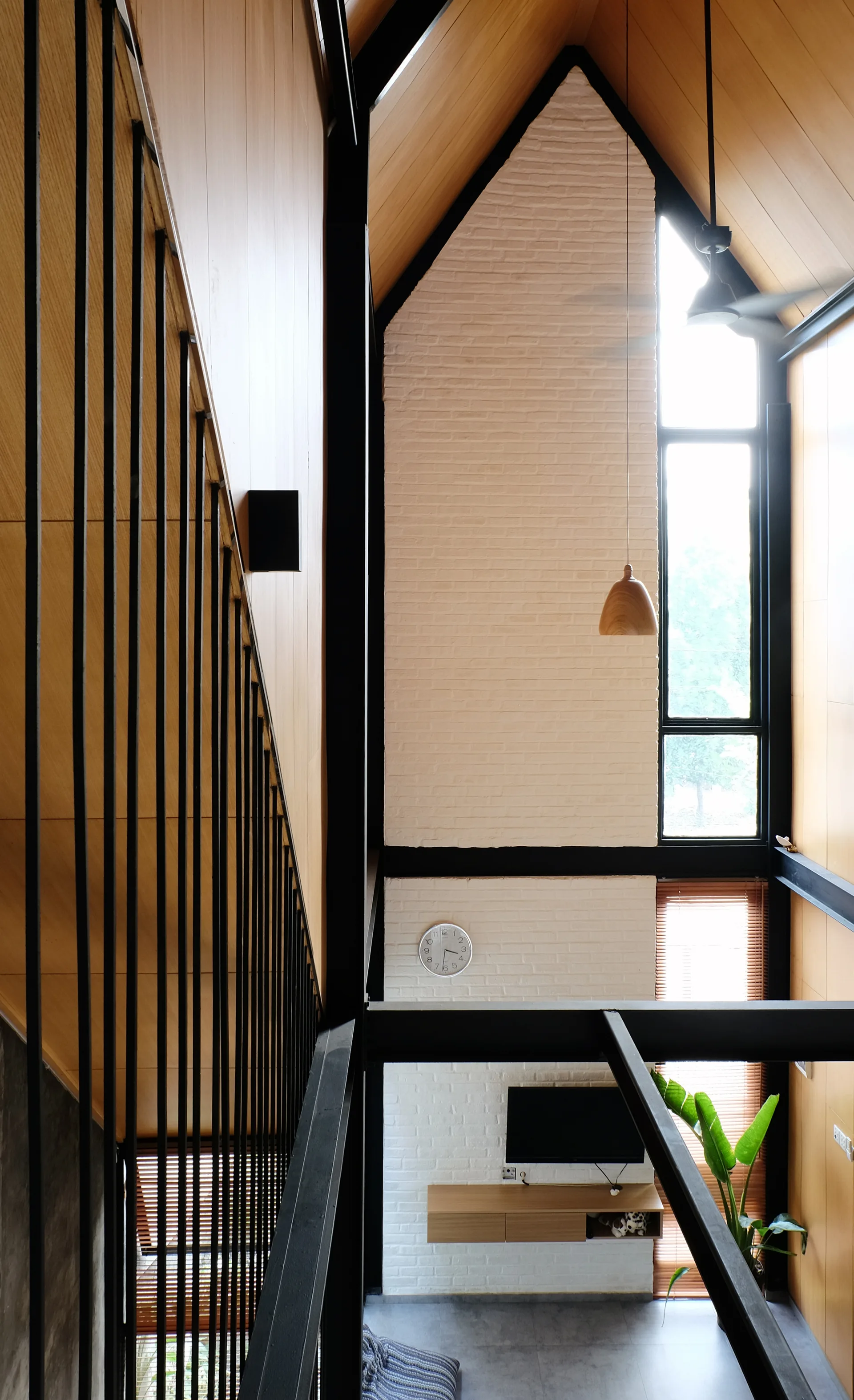 A high-angle view of a living space with a tall white brick wall, wood-paneled vaulted ceiling, and black metal staircase railings.