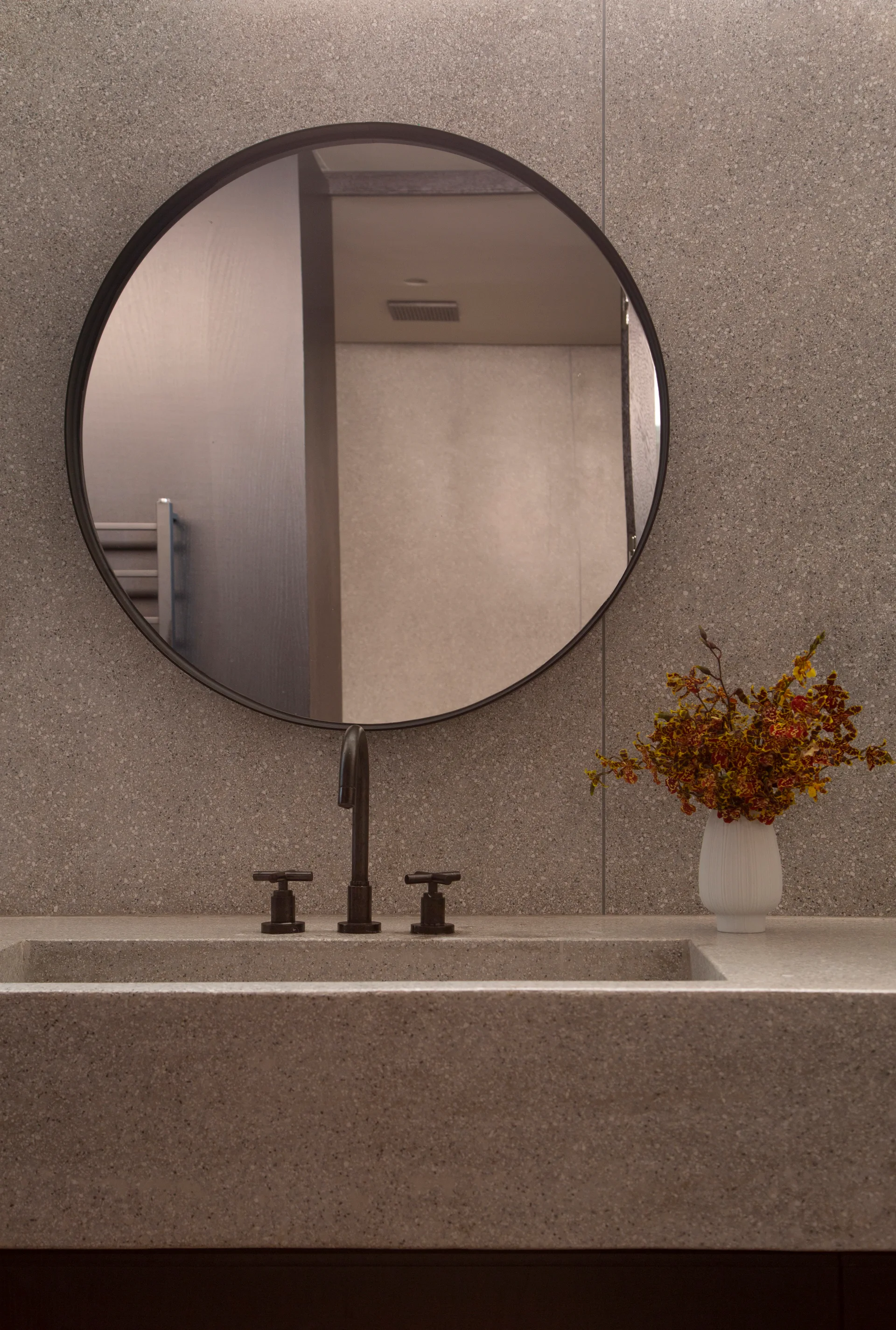 A modern bathroom vanity featuring an integrated speckled stone sink, matte black faucet, and a round black-framed mirror.