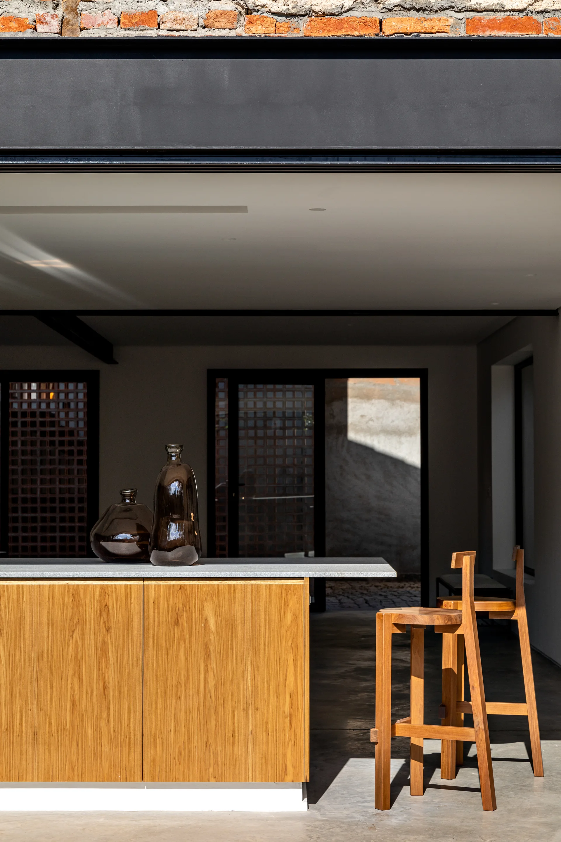 A modern wooden kitchen island with a grey stone-like countertop features two amber glass vases and sits next to two matching wooden bar stools.