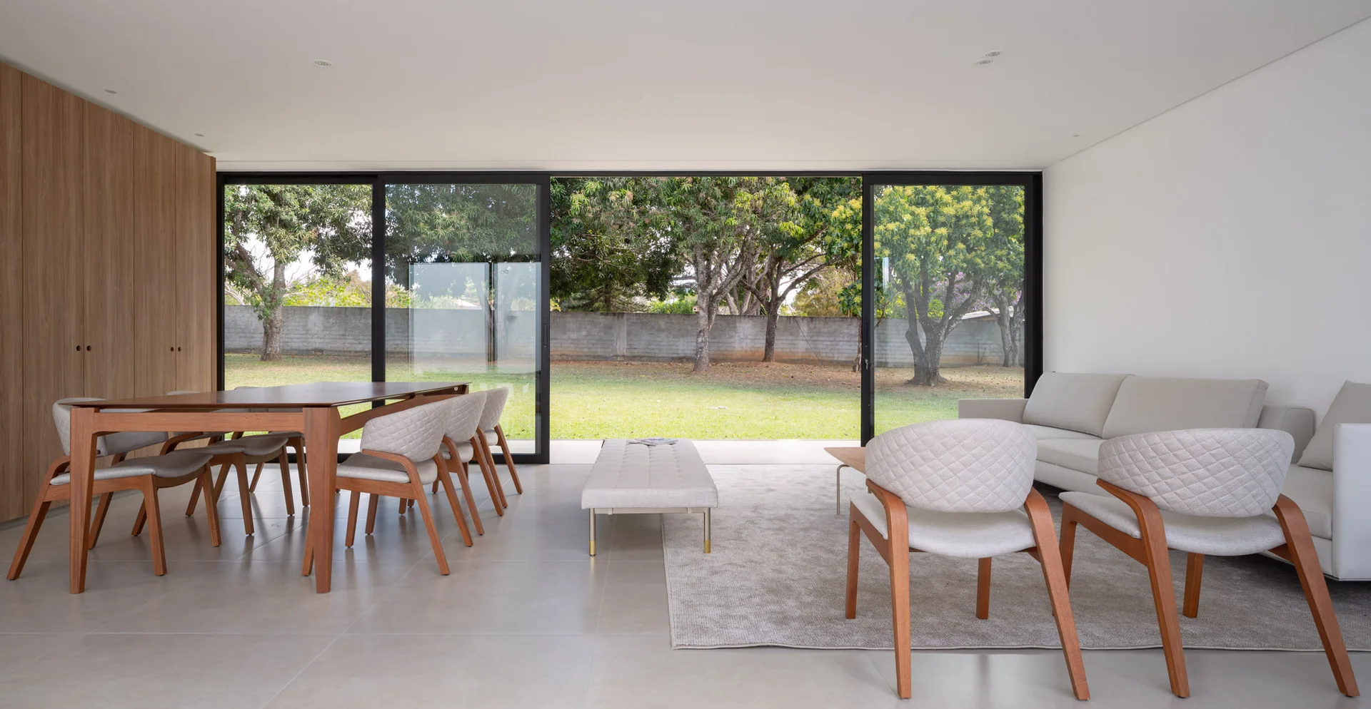 An open-concept living and dining area features a wooden dining set, quilted armchairs, and large sliding glass doors leading to a green yard.