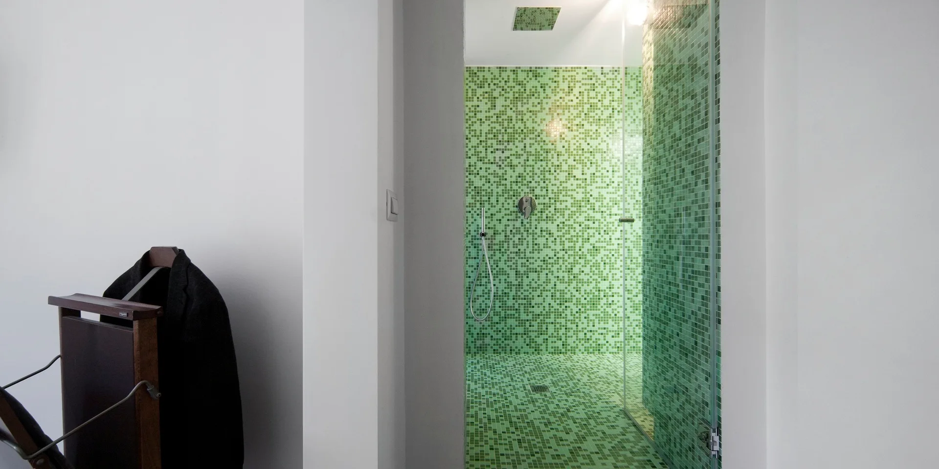 A modern bathroom featuring a walk-in shower lined in green mosaic tiles behind a clear glass door next to white walls.