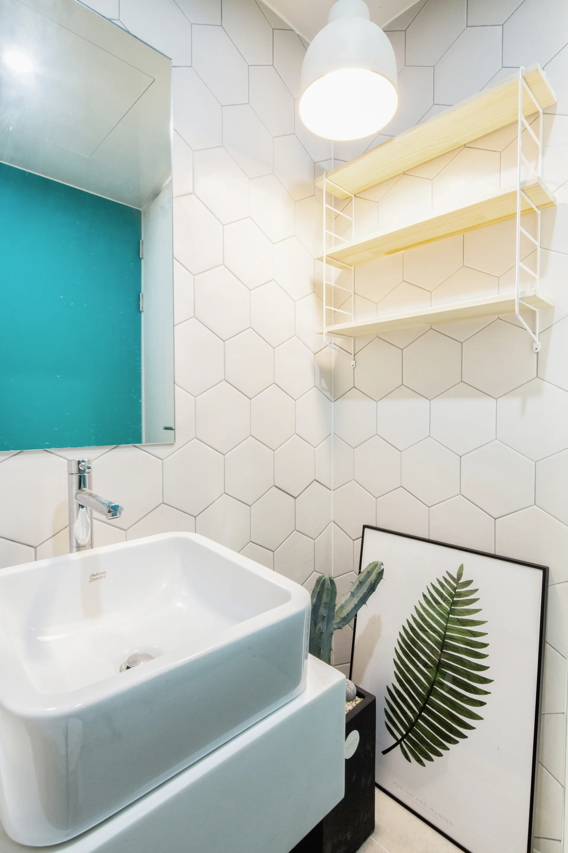 A bathroom vanity features a white square sink, chrome faucet, and a light wood shelving unit mounted on a white hexagonal tiled wall.