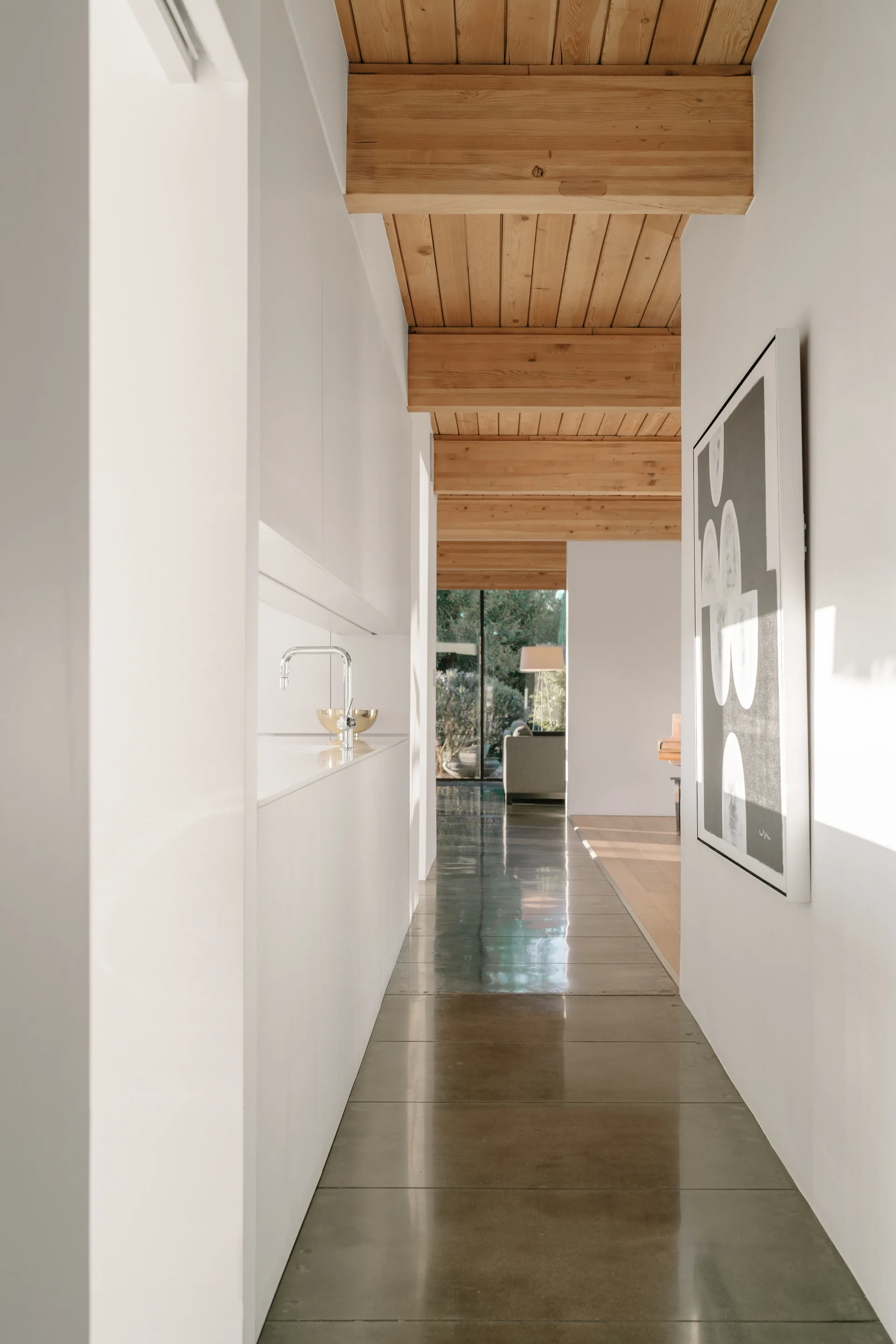 A minimalist hallway with polished concrete floors features flat-panel white cabinets and an exposed timber beam ceiling.
