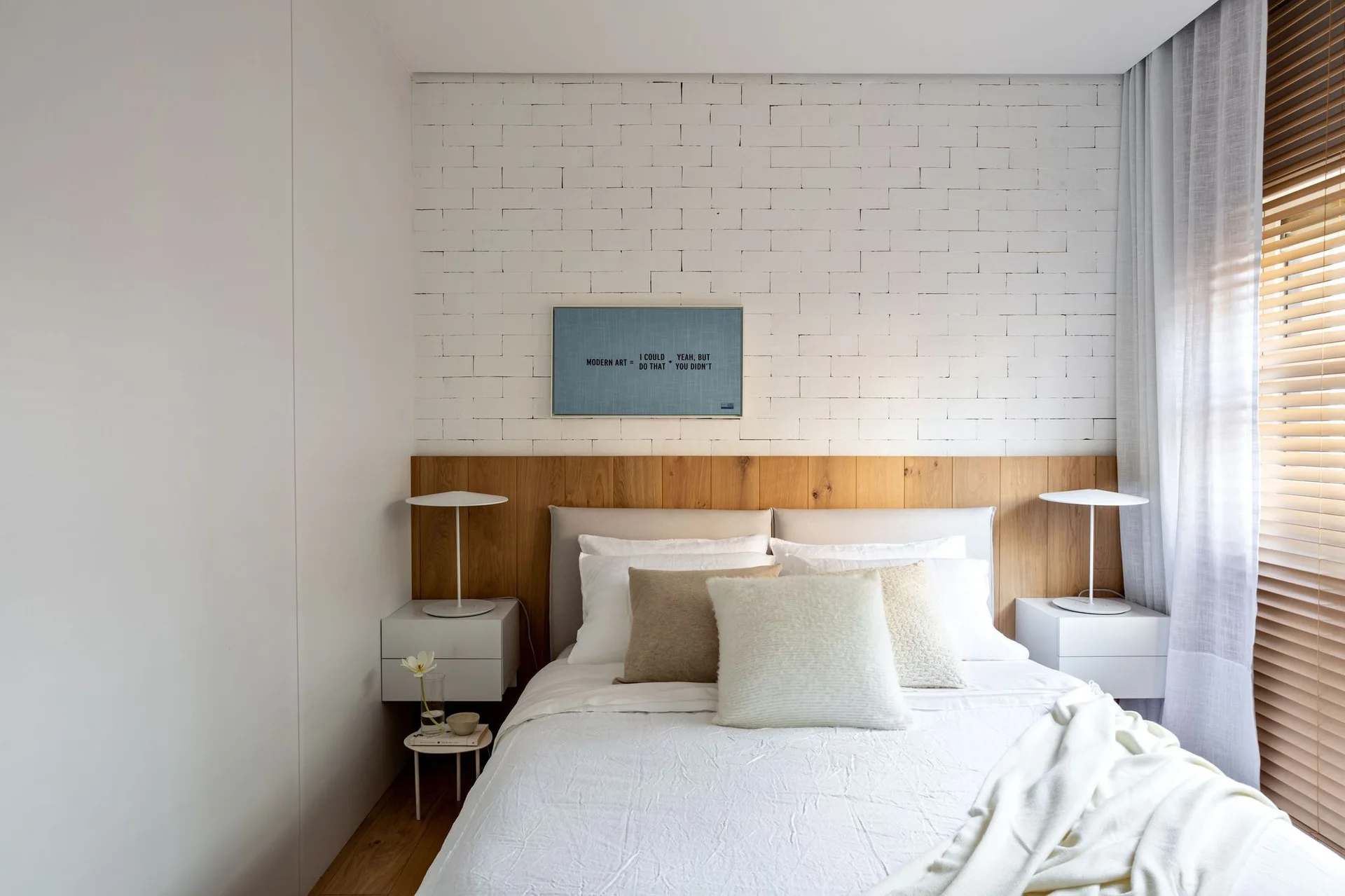 A minimalist bedroom features a bed with a white brick and wood paneled headboard wall, flanked by floating white nightstands and modern table lamps.