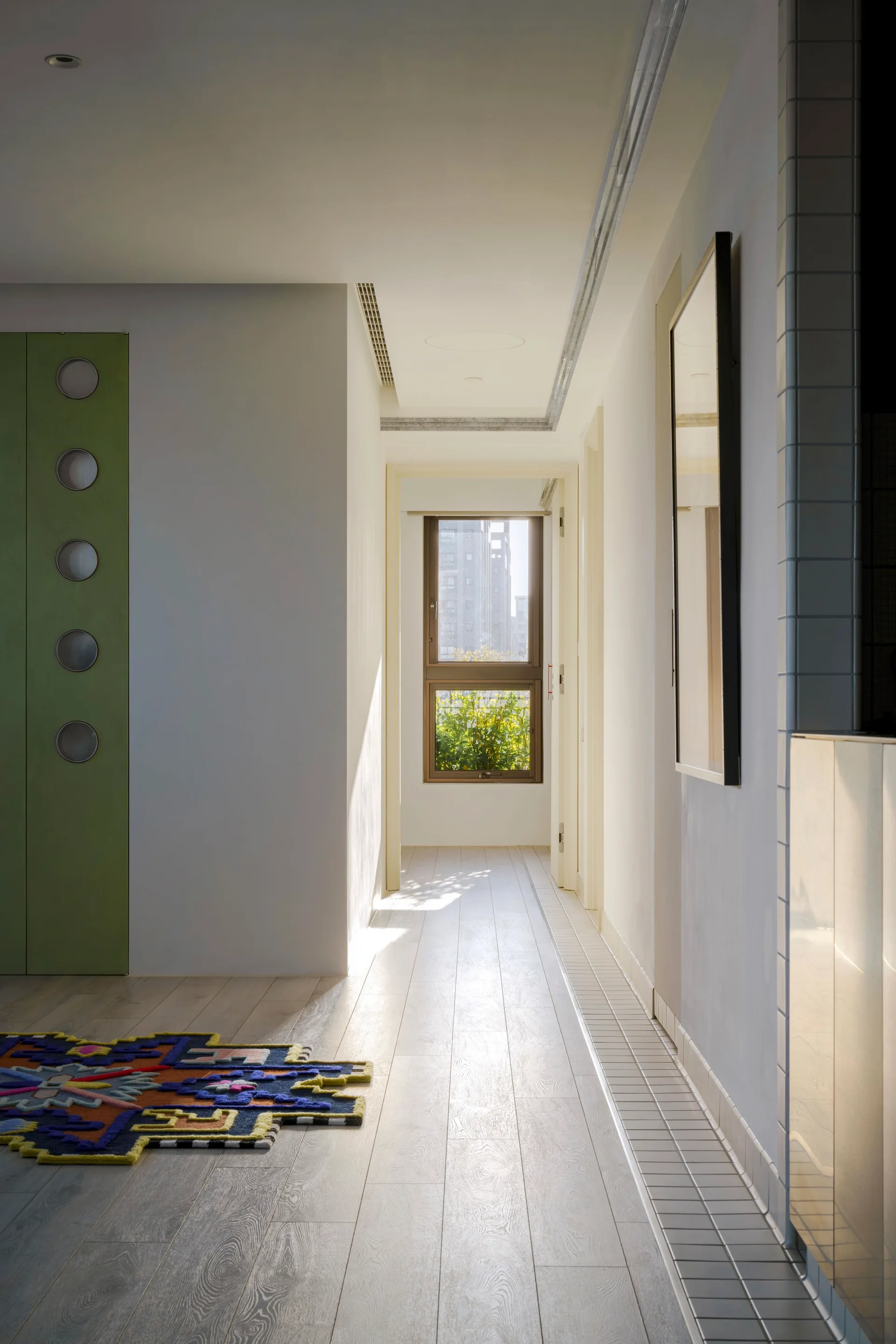 A bright hallway features light wood flooring, white walls, and a tall green door detailed with circular glass portholes.