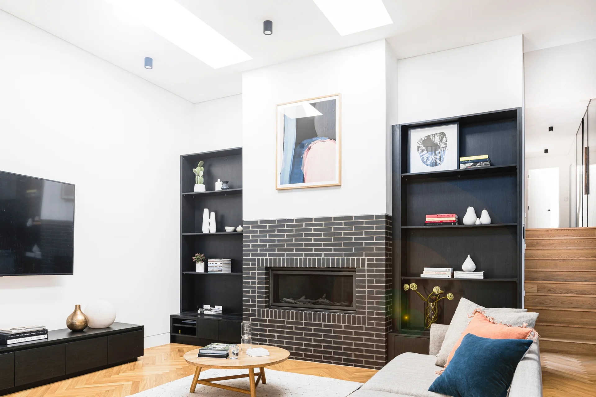 A modern living room features a dark brick fireplace flanked by black built-in bookshelves, a grey sofa, and herringbone pattern wood flooring.