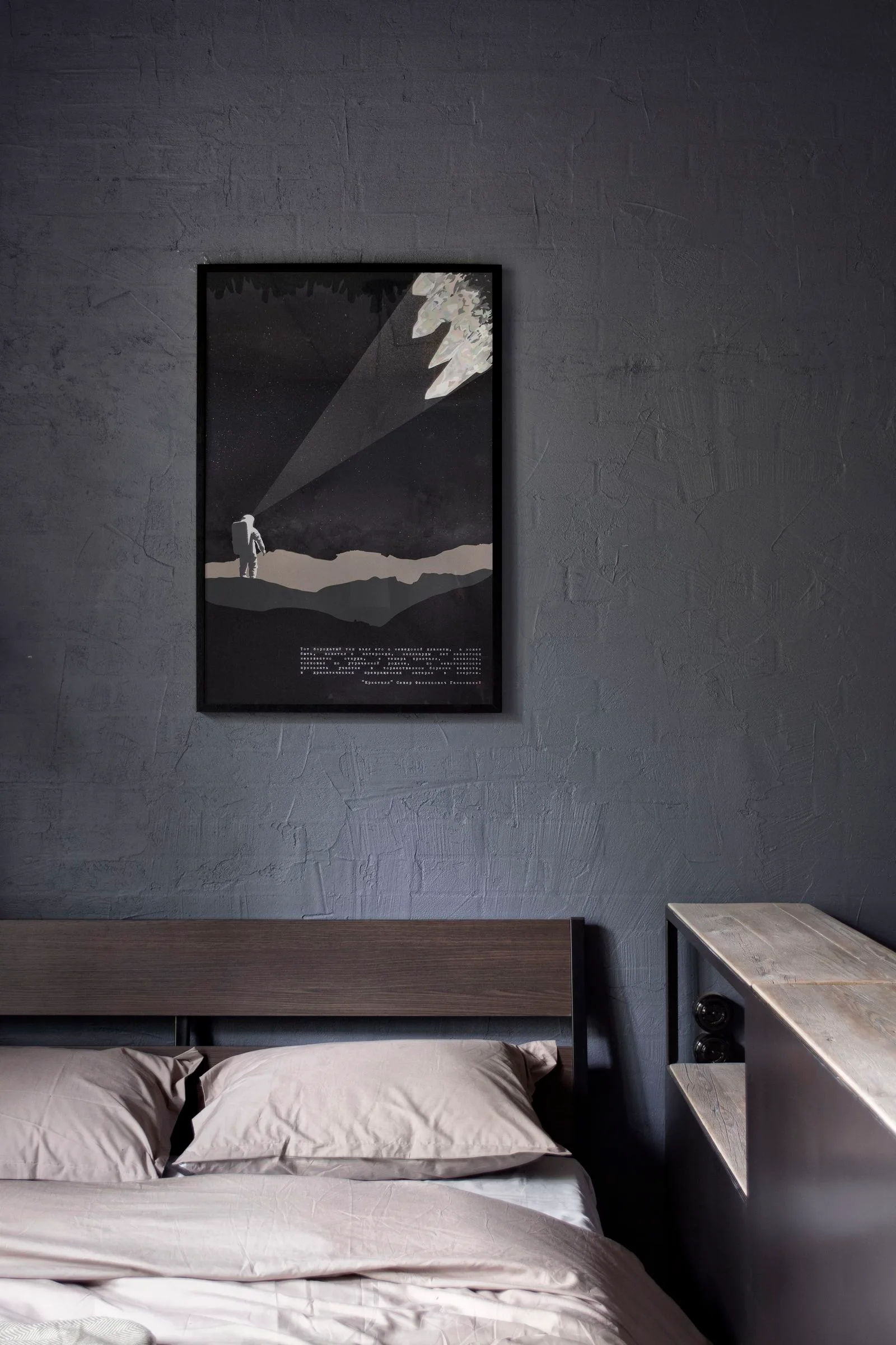 A framed space-themed print hangs on a textured charcoal plaster wall above a dark wood headboard and grey bedding in a bedroom.