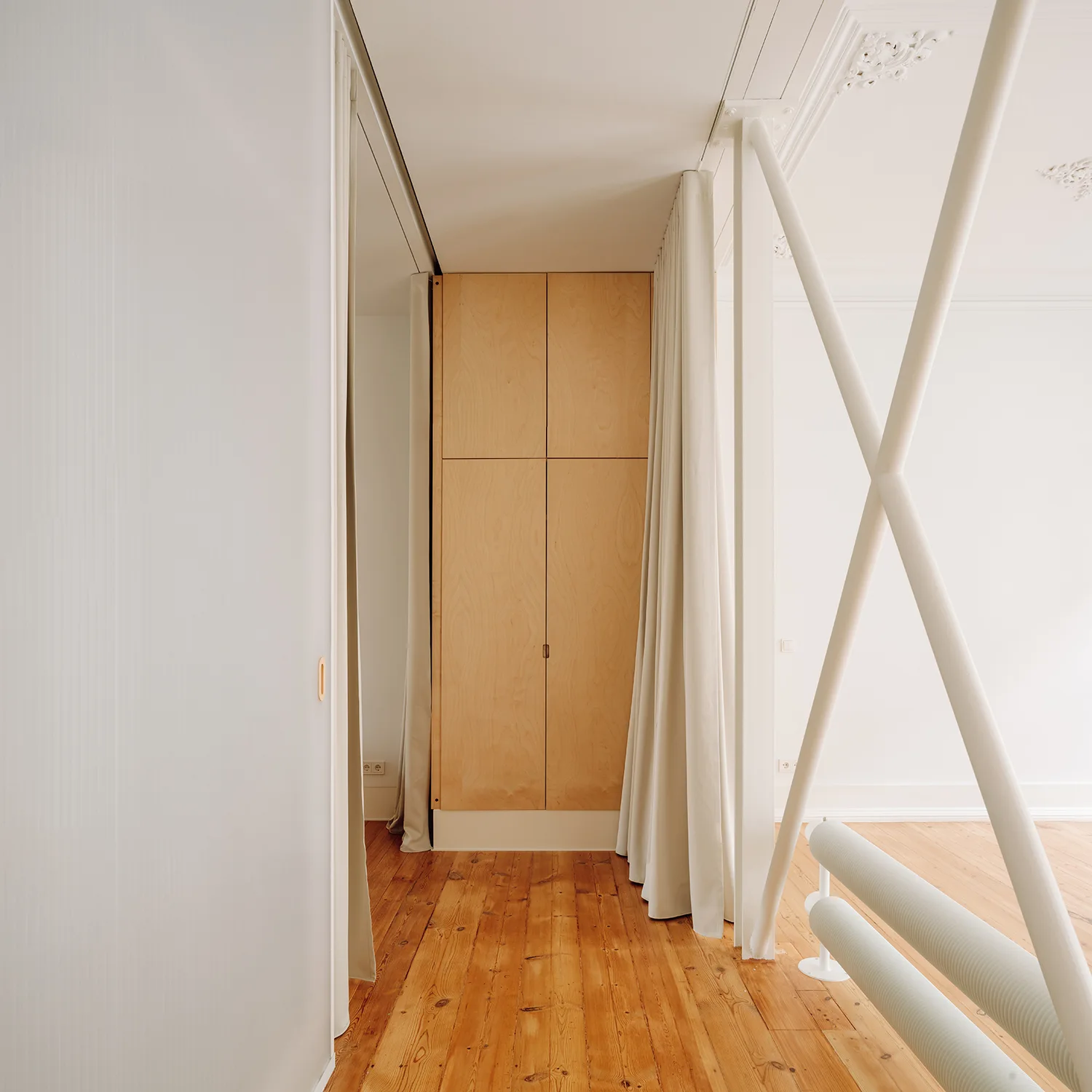 An interior room featuring tall plywood cabinets, white structural cross-bracing, warm wood flooring, and a fabric curtain room divider.
